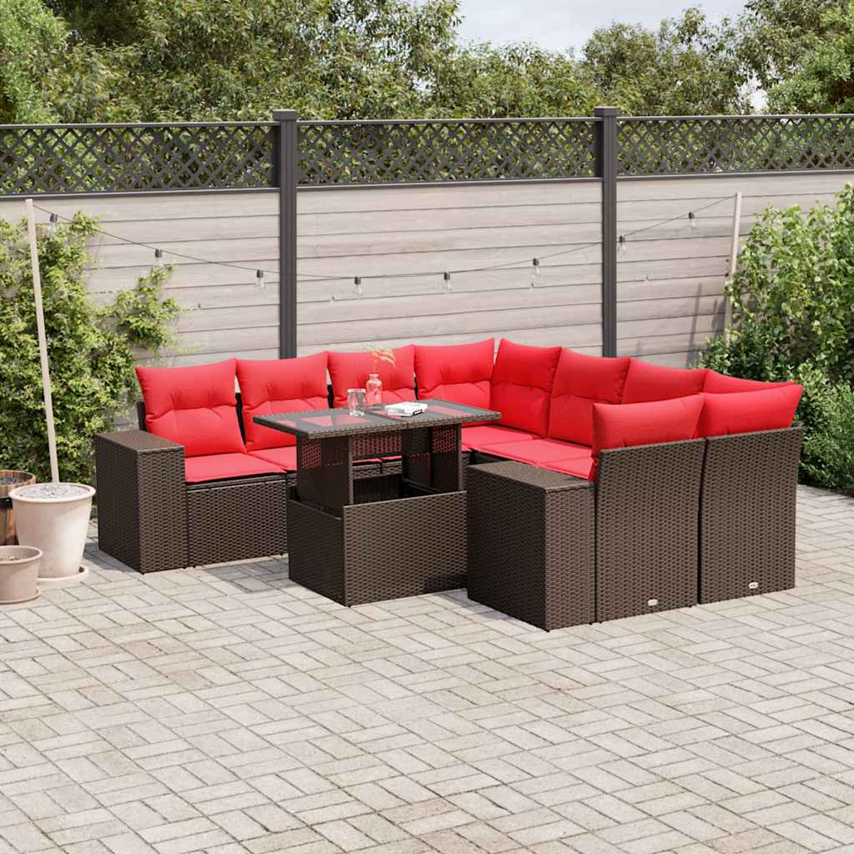 Outdoor-Ecksofa mit roten Kissen und einem Tisch mit Glasplatte auf einer Terrasse. Zaun und Pflanzen im Hintergrund.