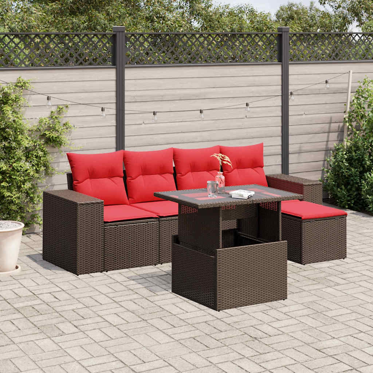 Outdoor-Terrassenset mit braunen Korbmöbeln und roten Kissen. Enthält ein Sofa, einen Tisch und eine Ottomane auf einer Steinterrasse.
