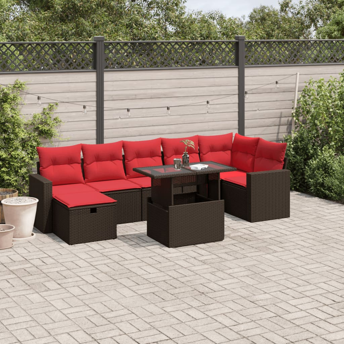 Garten-Terrassenset mit roten Kissen, einem Tisch mit Glasplatte und einer gefliesten Terrasse. Ein Zaun und Grün im Hintergrund.