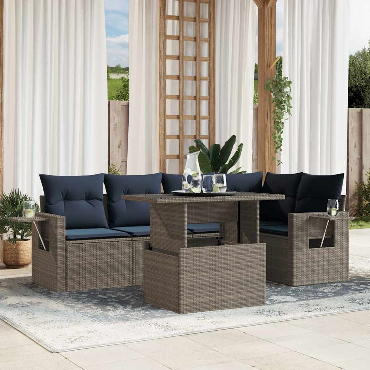 Outdoor-Terrassenset. Korbmöbel mit blauen Kissen, Tisch, Teppich, weißen Vorhängen und Grün im Hintergrund.
