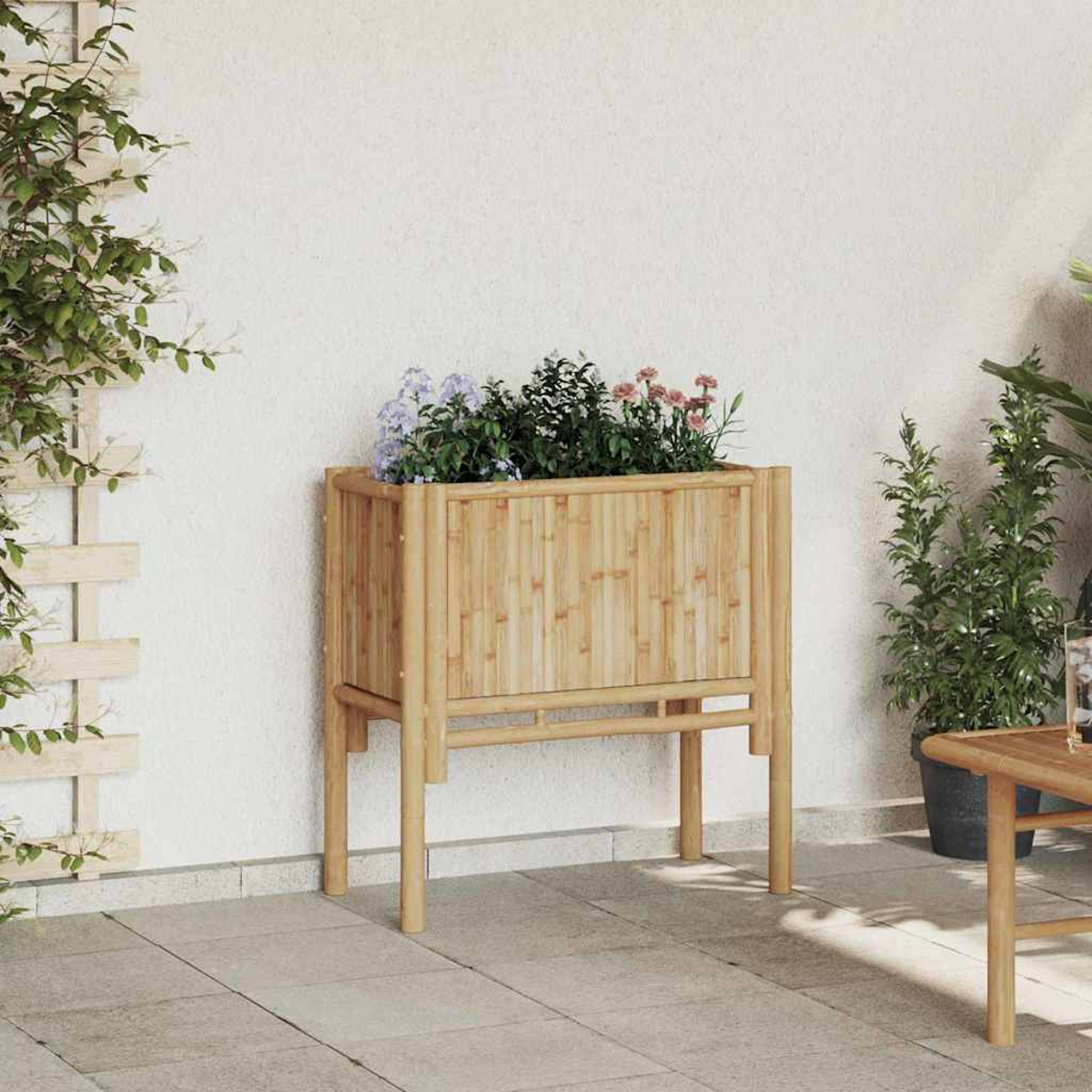 Una fioriera in bambù con fiori su un patio. Piante verdi e un tavolo sullo sfondo, e una pianta rampicante a sinistra.