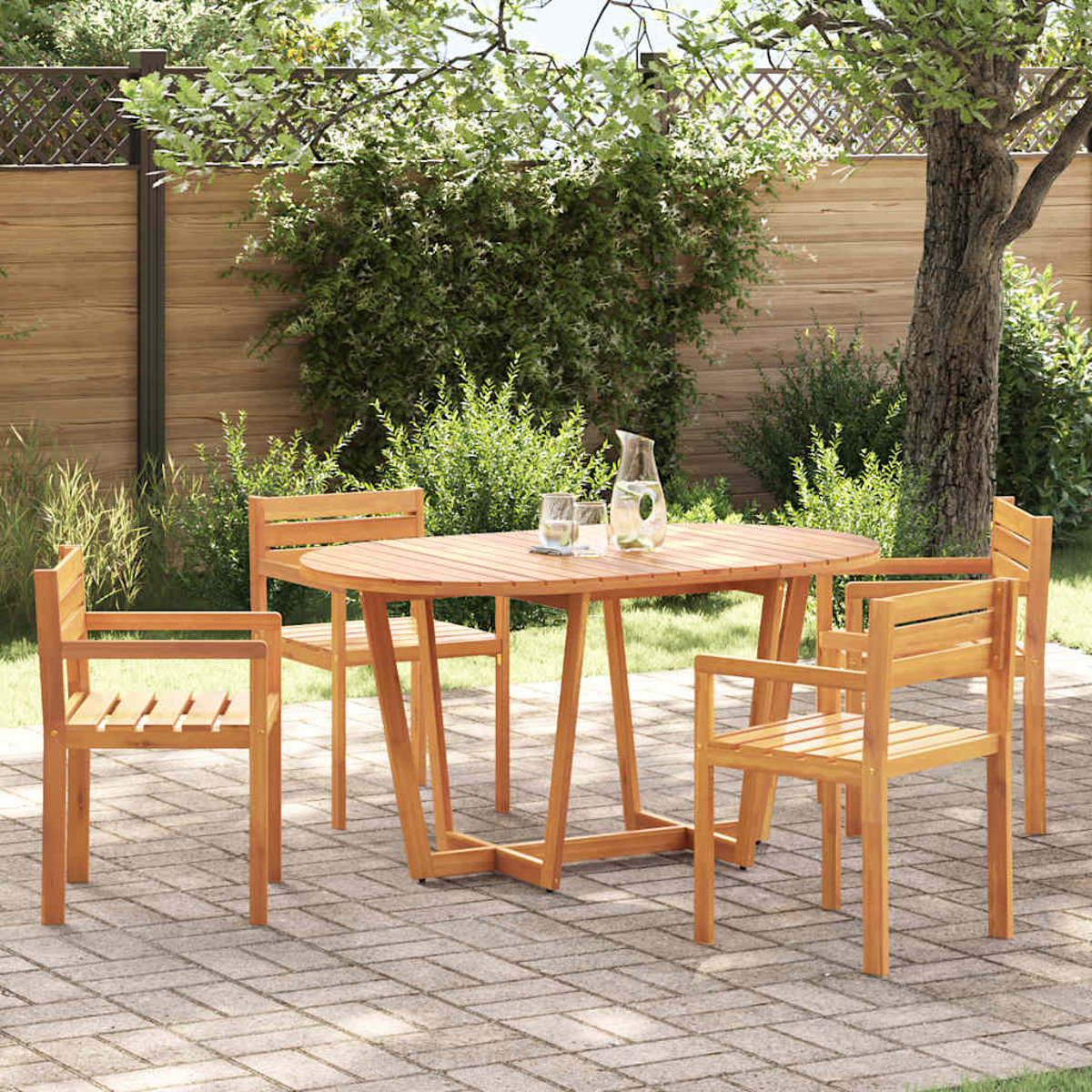Ein Holz-Terrassenset mit Tisch und Stühlen steht auf einer Backsteinterrasse. Im Hintergrund ein Zaun, üppiges Grün und ein Baum.