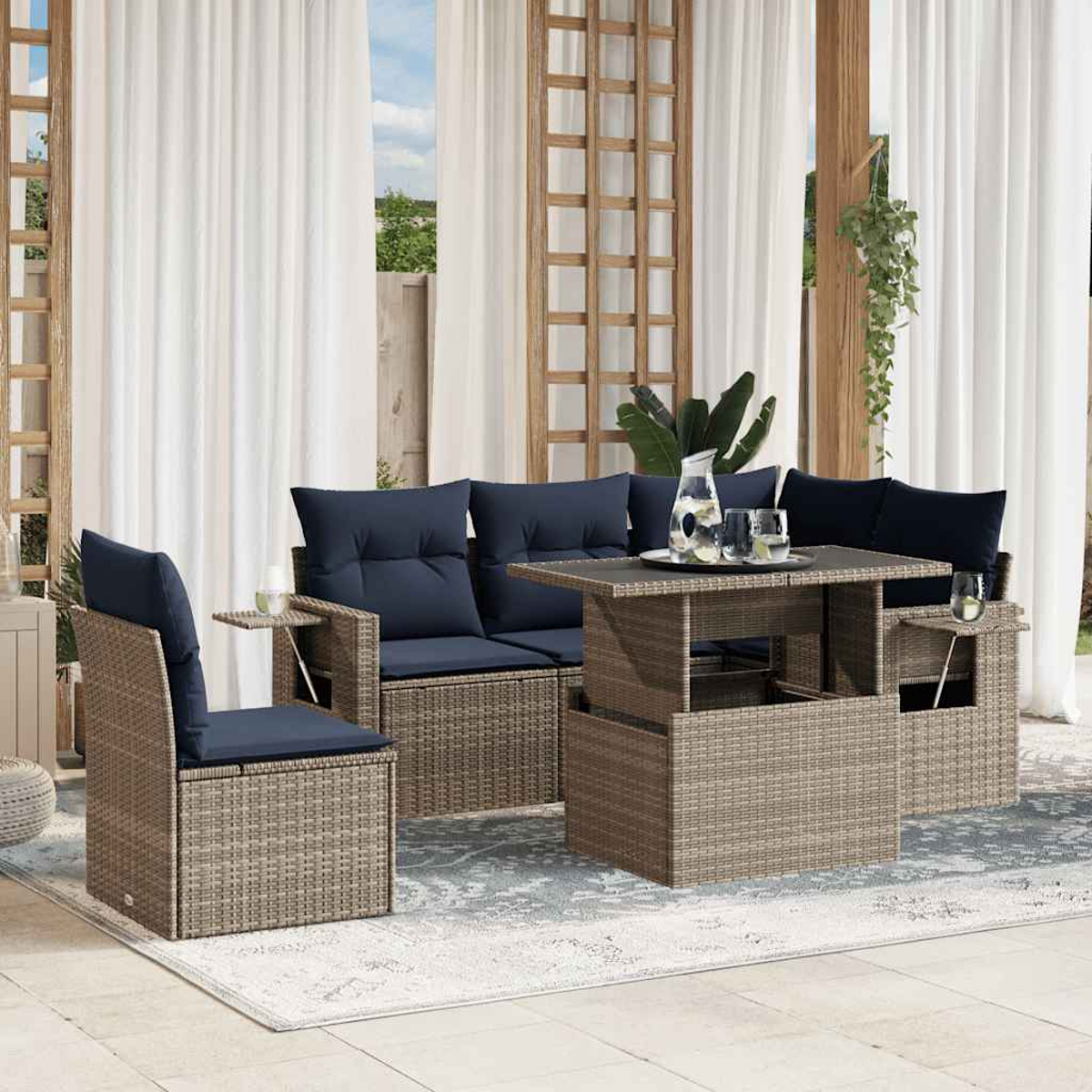 Gartenmöbel-Set aus Korbgeflecht mit marineblauen Kissen, einem Aufstehtisch und Gläsern auf einem Teppich, mit weißen Vorhängen im Hintergrund.