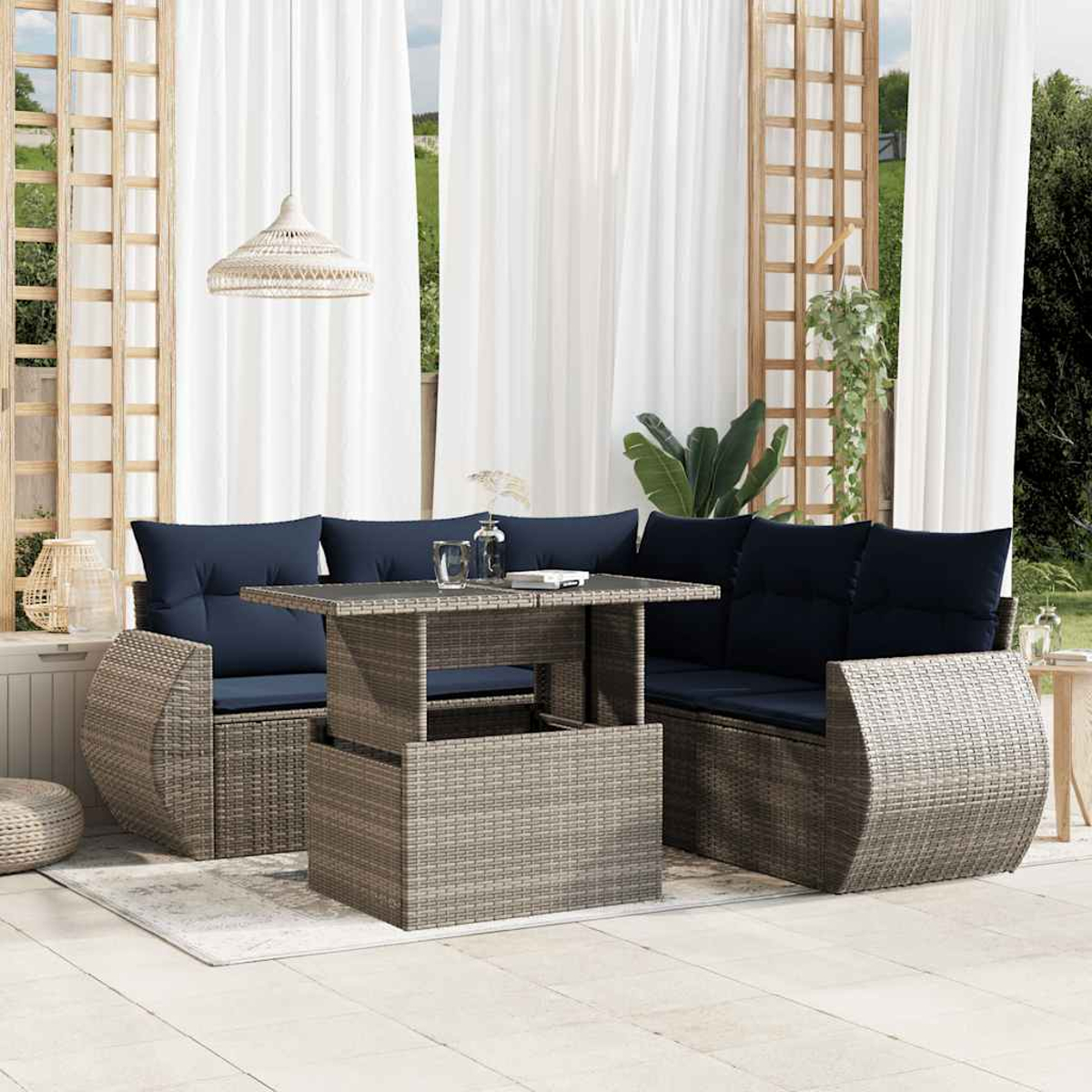 Terrassenmöbel-Set im Freien mit grauen Korbmöbeln, marineblauen Kissen, einem Tisch und weißen Vorhängen. Eine dekorative Lampe hängt darüber.