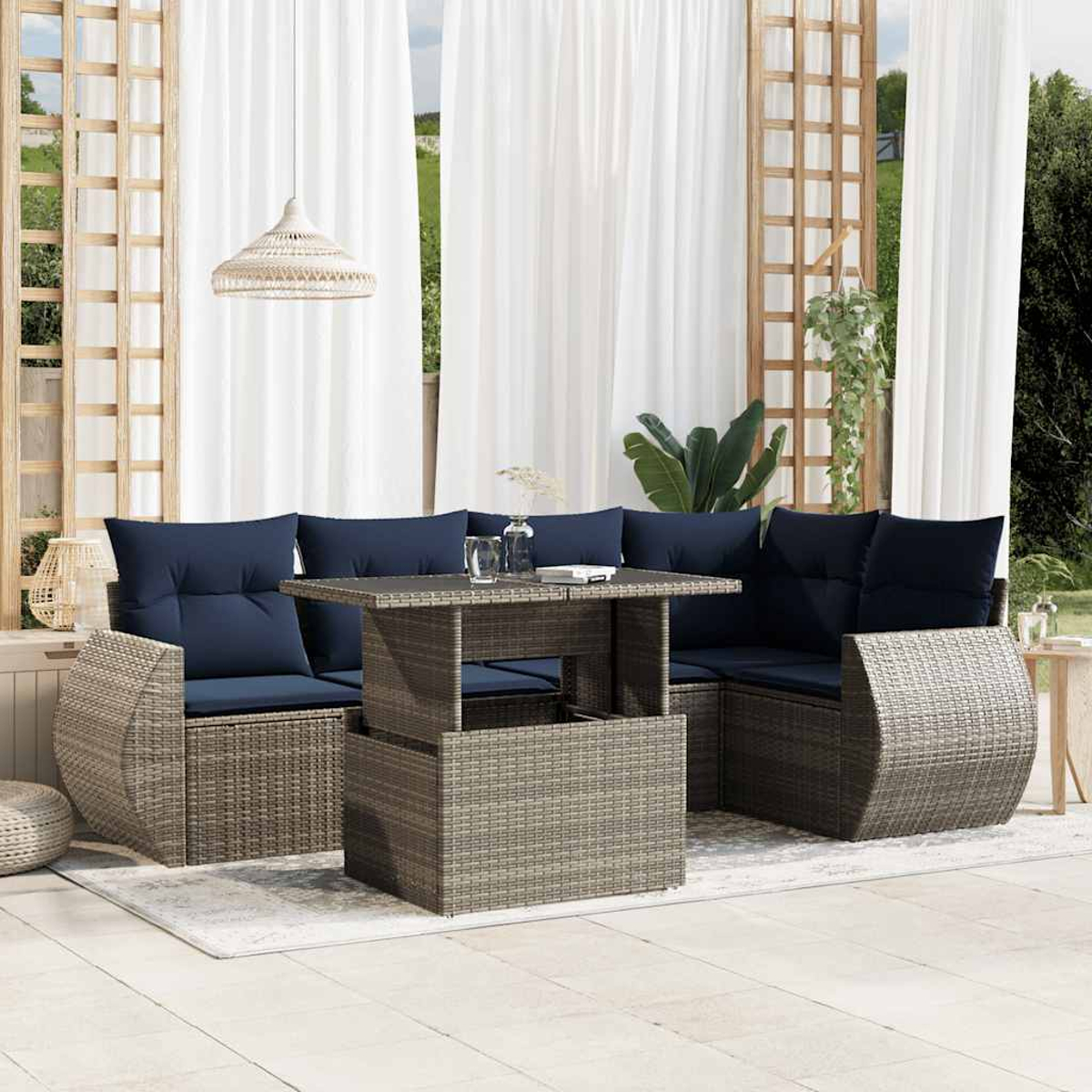Terrassenset im Freien mit Korbmöbeln, blauen Kissen und einem Hebetisch. Weiße Vorhänge und Grün im Hintergrund.