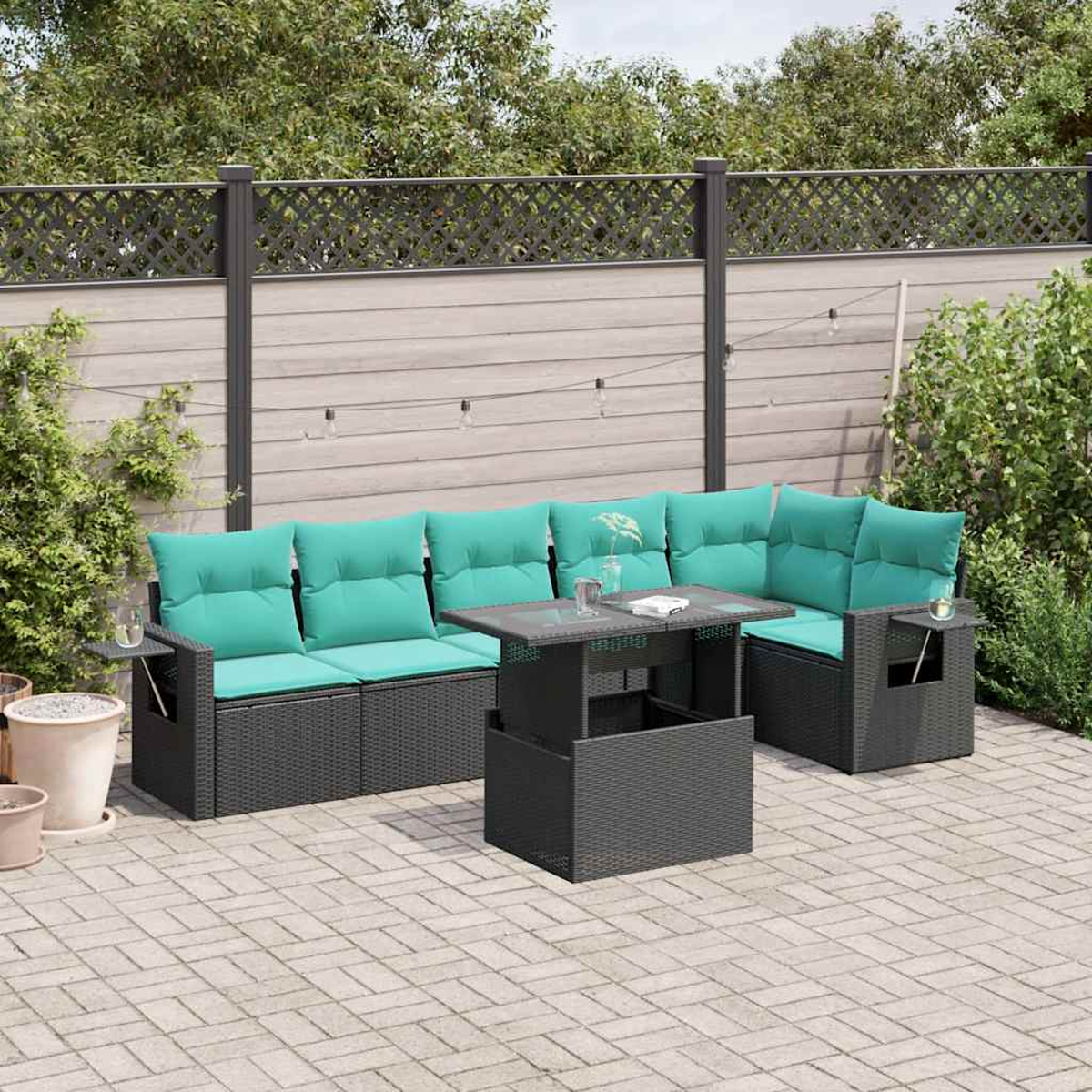 Gartenmöbel-Set mit tealfarbenen Kissen, einem schwarzen Tisch und einem Zaun im Hintergrund. Die Szene befindet sich auf einer gepflasterten Terrasse.