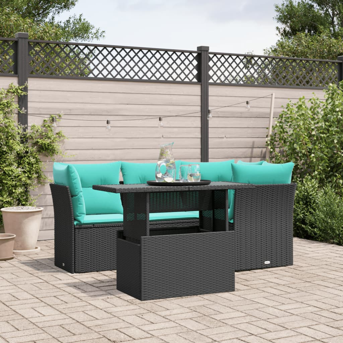 Terrassenmöbel-Set mit schwarzer Korbgeflecht-Garnitur, türkisfarbenen Kissen, Glastisch und einem verzierten Zaun im Hintergrund.