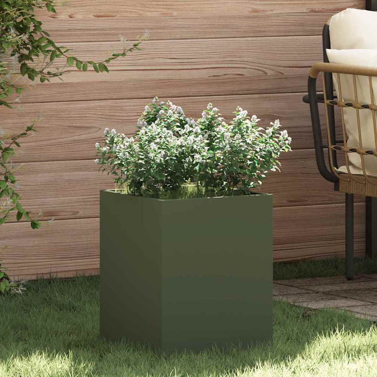 Una fioriera verde quadrata con piante da fiore bianche si trova sull'erba. Sullo sfondo un muro di legno e una sedia.