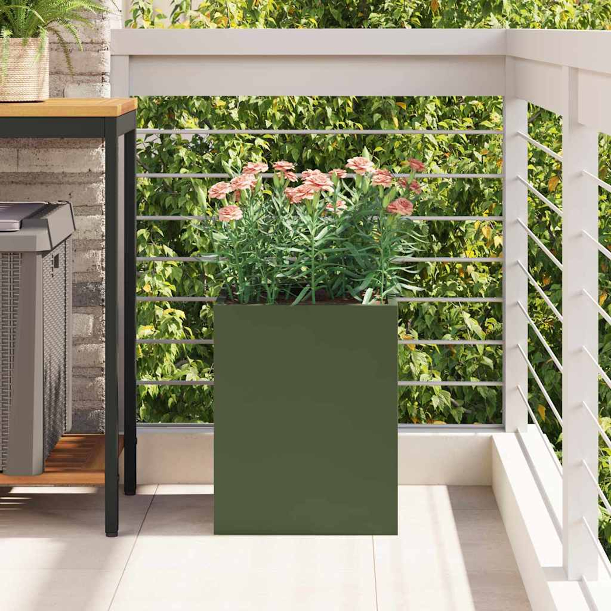 Una fioriera verde su un balcone con fiori rosa. Ringhiera bianca e verde sullo sfondo. Un tavolo a sinistra.