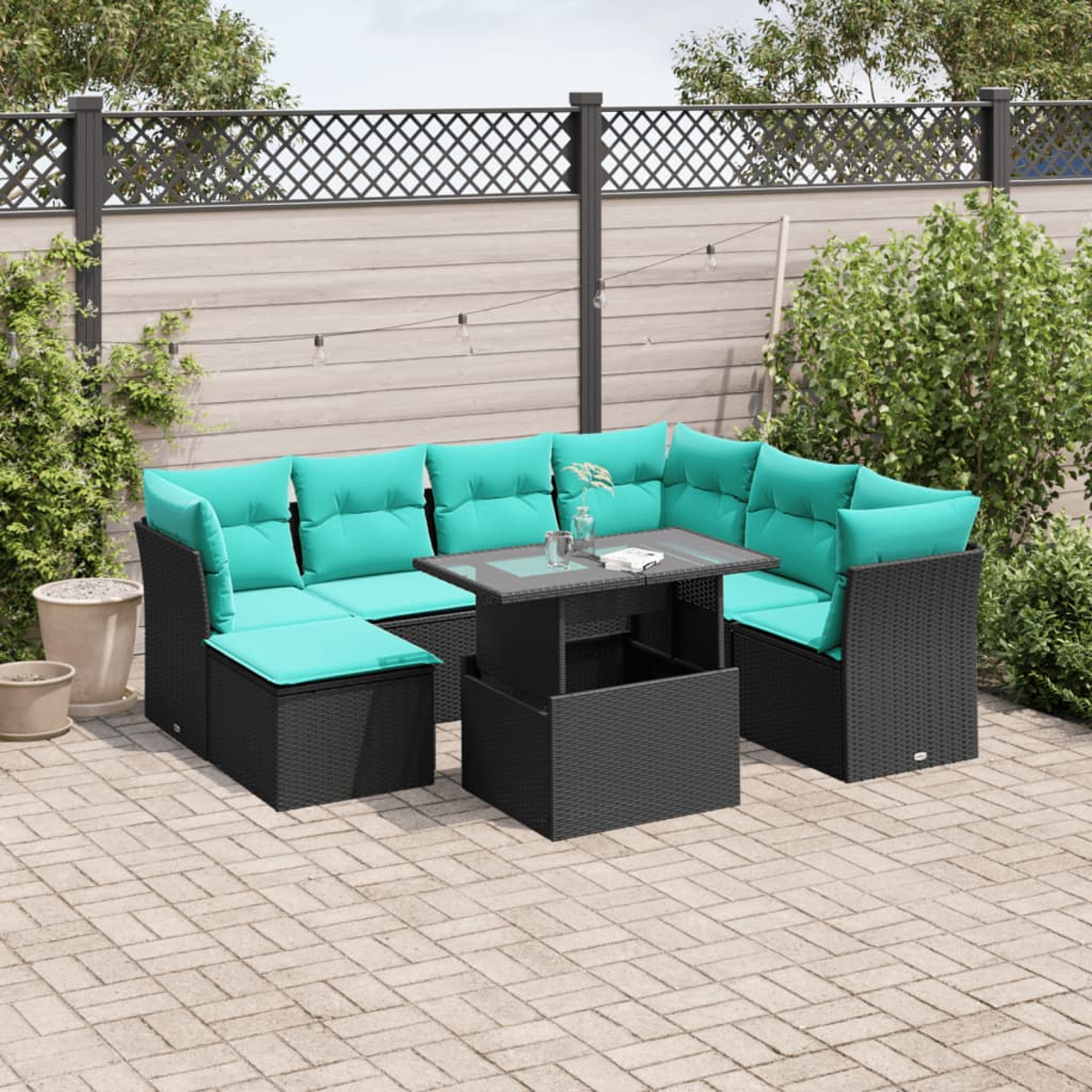 Outdoor-Sitzgruppe mit türkisfarbenen Kissen und schwarzem Korbgeflecht. Enthält einen Tisch mit Glasplatte. Auf einer Ziegelterrasse mit Zaun.