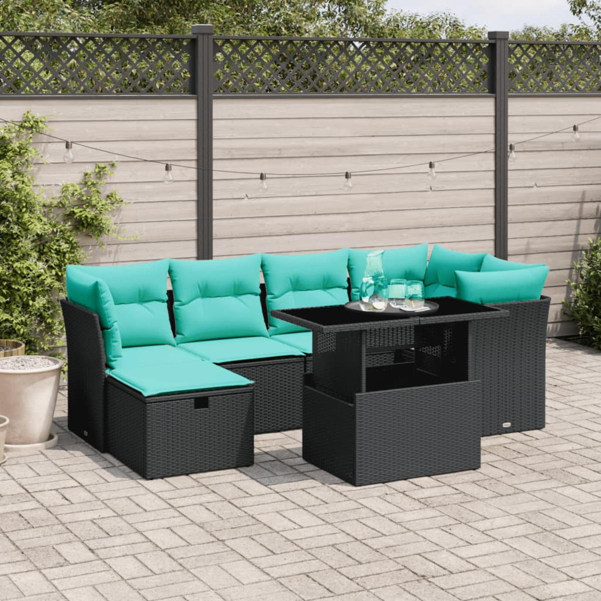 Garten-Terrassenset mit schwarzem Korbmöbel und türkisfarbenen Kissen. Ein schwarzer Tisch trägt Gläser. Der Hintergrund zeigt einen Zaun und Pflanzen.