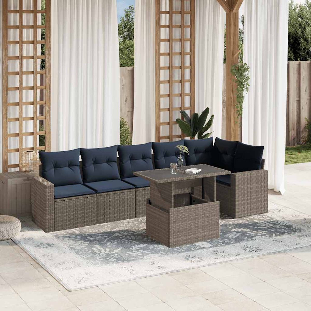 Garten-Sitzgruppe mit blauen Kissen auf einem gemusterten Teppich. Ein Tisch mit Hubfunktion steht davor. Weiße Vorhänge und Holzkonstruktion.