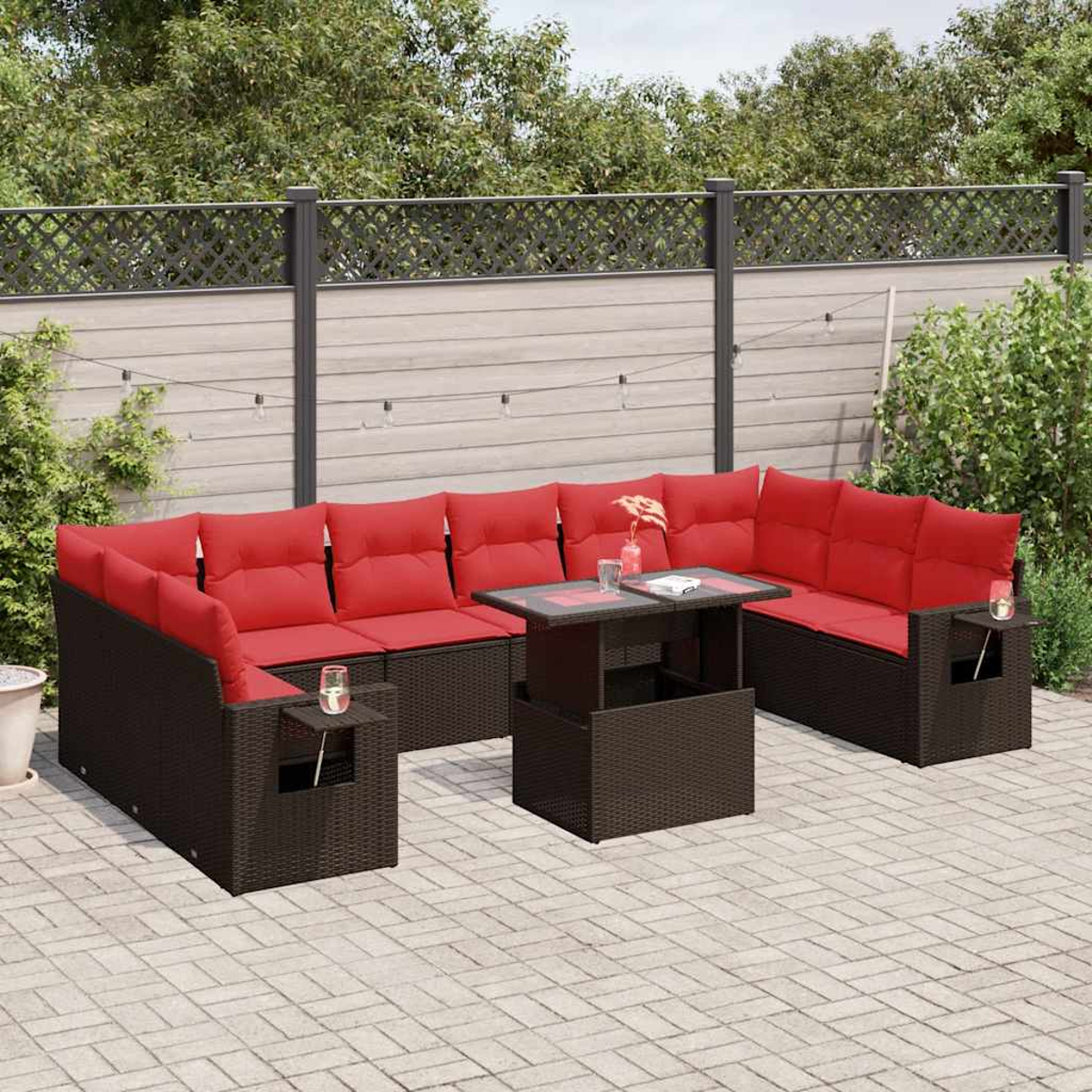 Outdoor-Ecksofa mit roten Kissen und einem Tisch mit Glasplatte. Auf einer gepflasterten Terrasse mit Zaun und Grün im Hintergrund.