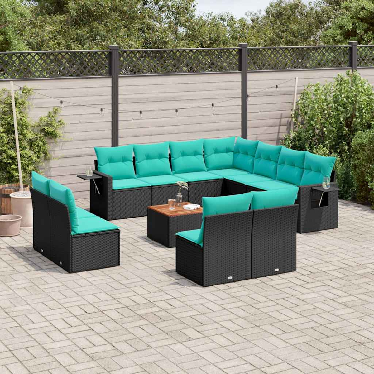 Terrassengarnitur mit schwarzem Korbmöbeln, türkisfarbenen Kissen und einem Holztisch. Auf einer Backsteinterrasse mit Holzzaun im Hintergrund.