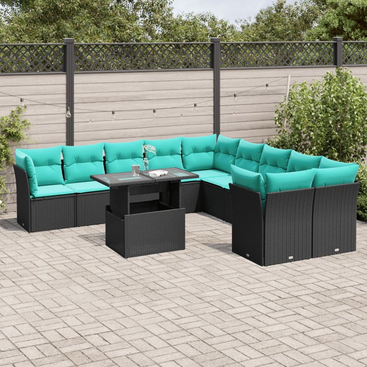 Outdoor-Ecksofa mit türkisfarbenen Kissen und einem schwarzen Tisch. Auf einer Terrasse aufgestellt. Im Hintergrund befinden sich ein Zaun und Grün.
