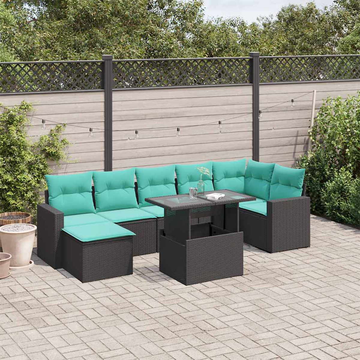 Garten-Terrassenset mit dunkelgrauen Korbmöbeln und tealfarbenen Kissen. Ein Tisch mit Glasplatte steht in der Mitte. Ein Holzzaun im Hintergrund.