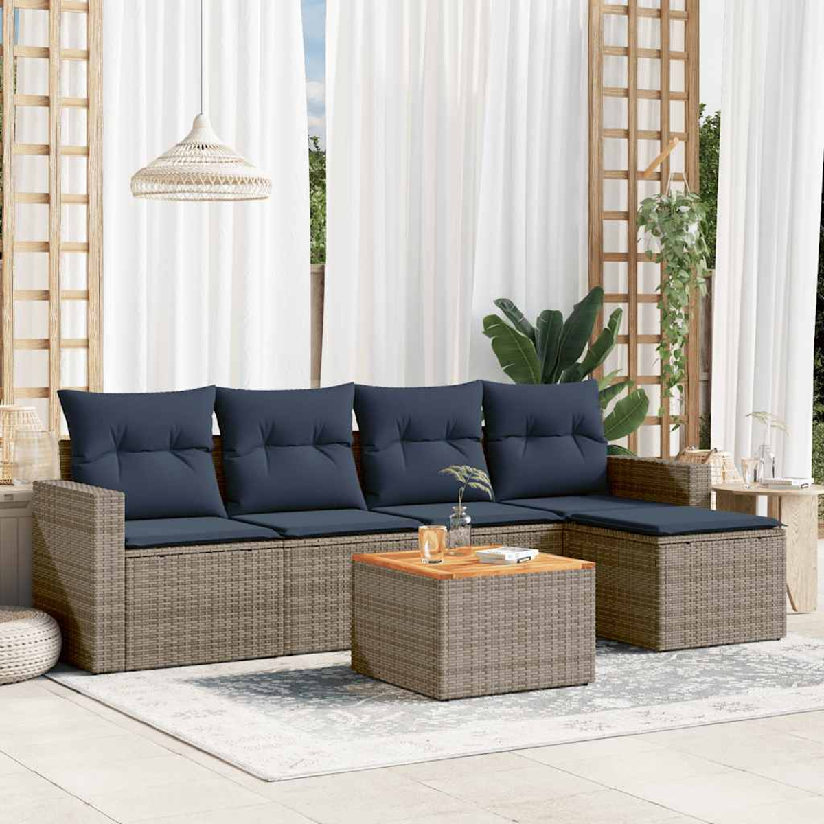 Wohnzimmer im Freien mit grauem Korbmöbel, marineblauen Kissen, Holztisch, weißen Vorhängen und einer Hängelampe.