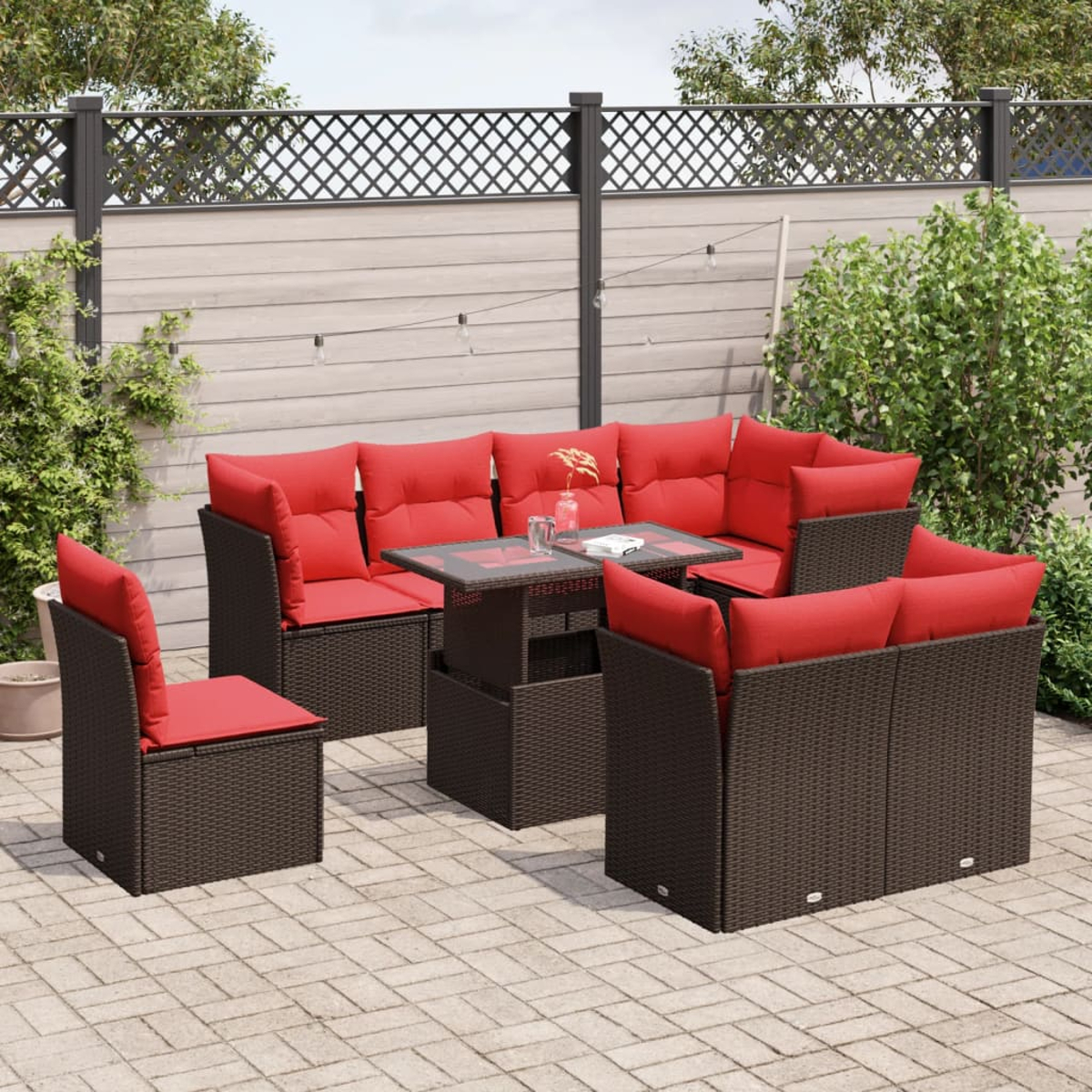 Gartenmöbel-Set mit braunen Korbgeweben und roten Kissen, einschließlich Tisch, Stühlen und Sofa, auf einer Steinterrasse.
