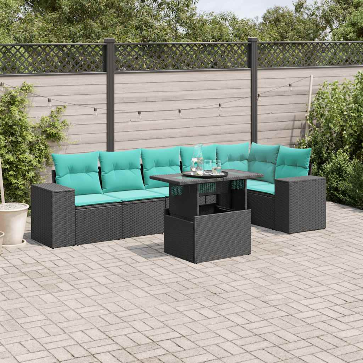 Garten-Set mit grauen Korbmöbeln, türkisfarbenen Kissen und einem Tisch. Es steht auf einer Ziegelterrasse mit Zaun im Hintergrund.