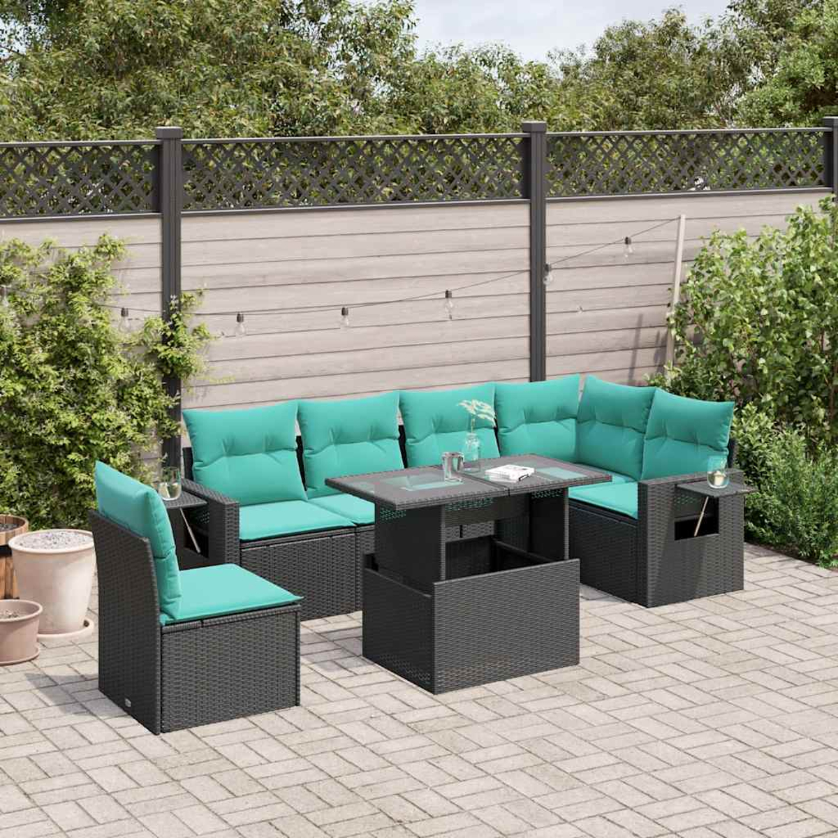 Terrassenmöbel-Set im Freien mit türkisfarbenen Kissen und einem Tisch mit Glasplatte, auf einer gepflasterten Terrasse, mit Holzzaun und Grün im Hintergrund.