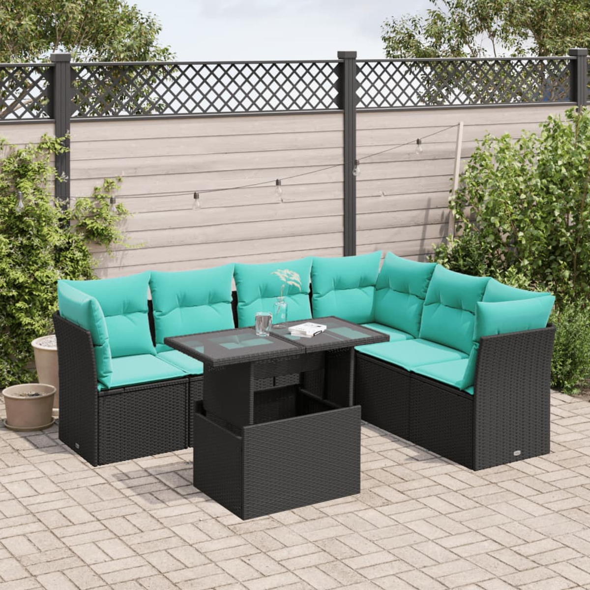 Gartensektionssofa mit türkisfarbenen Kissen und einem Tisch mit Glasplatte auf einer Ziegelterrasse. Ein Zaun und Grünzeug im Hintergrund.