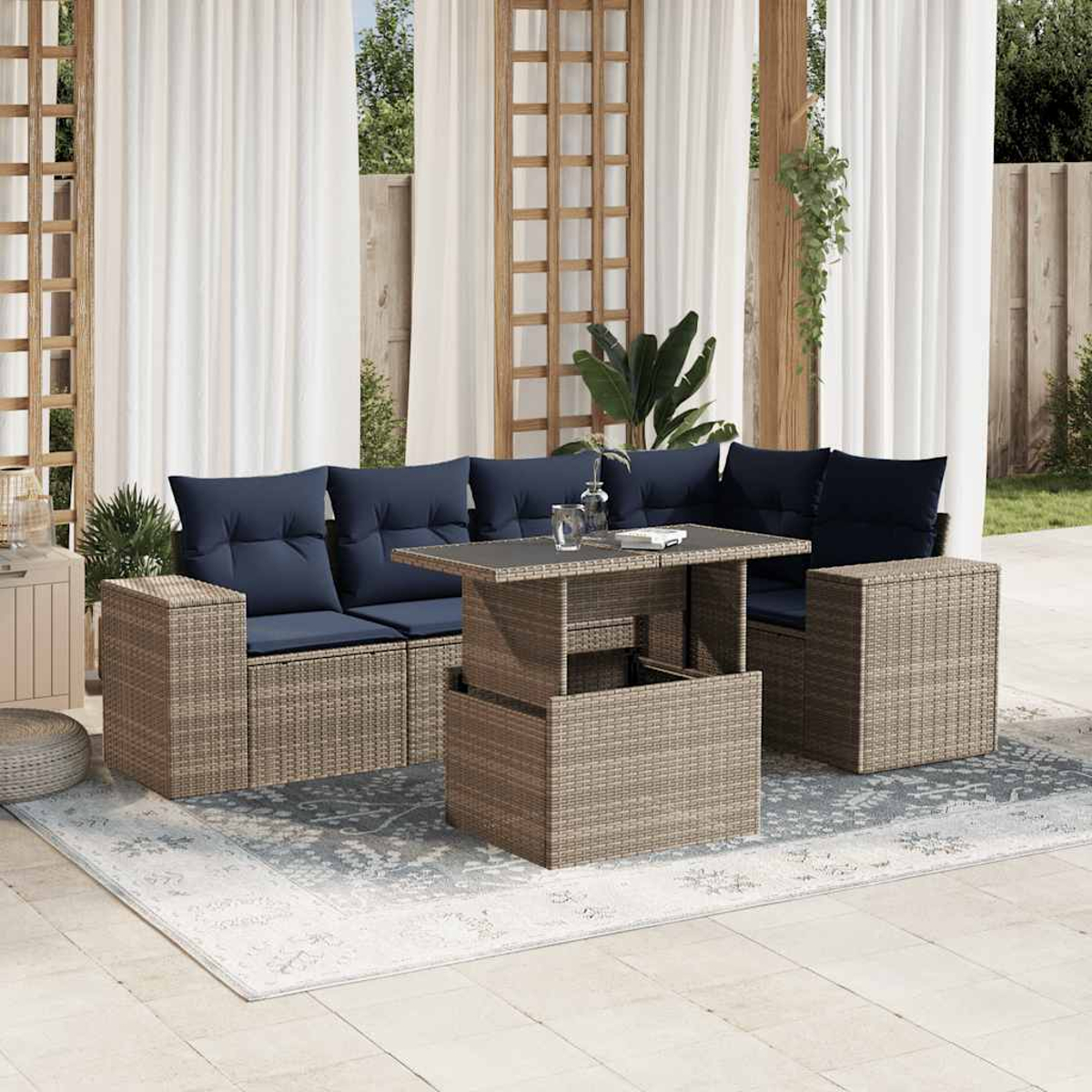 Terrassenset. Korbmöbel mit blauen Kissen. Tisch und Stühle auf einem gemusterten Teppich. Weiße Vorhänge und grüne Pflanzen.