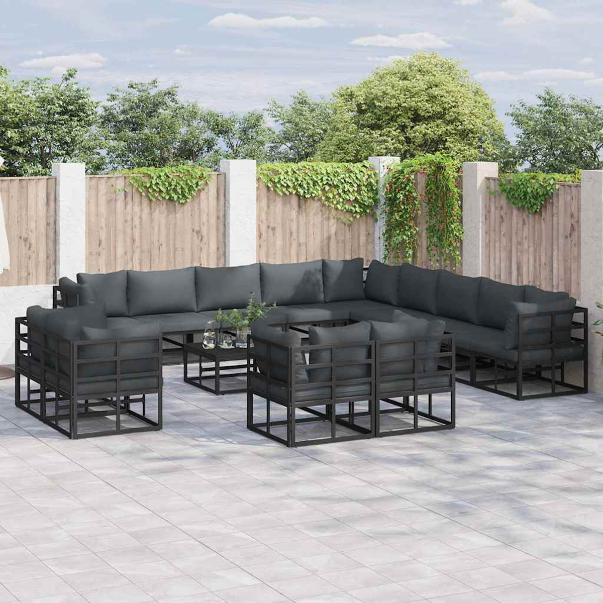 Gartenmöbel-Set auf einer Terrasse. Enthält grau gepolsterte Sofas und Stühle, einen Tisch mit Glasplatte und einen Holzzaun im Hintergrund.