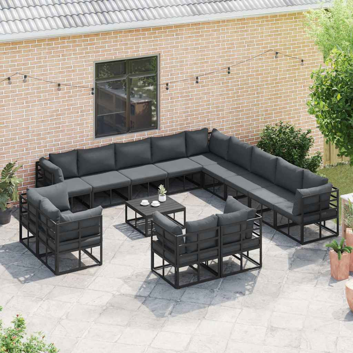 Gartenmöbel-Set. Graue Kissen auf schwarzen Metallrahmen. Couchtisch, Backsteinmauer im Hintergrund und Zierpflanzen.