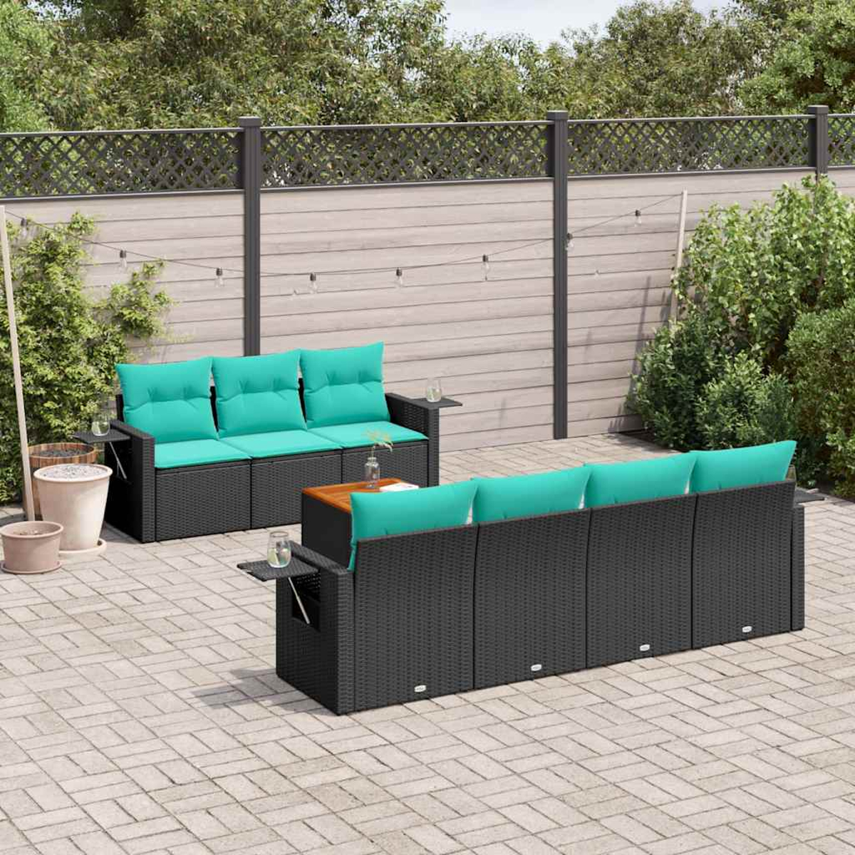 Terrassenmöbel-Set. Schwarze Korbsessel mit türkisfarbenen Kissen. Beistelltisch aus Holz. Ziegel-Patio, Holzzaun und Grün im Hintergrund.