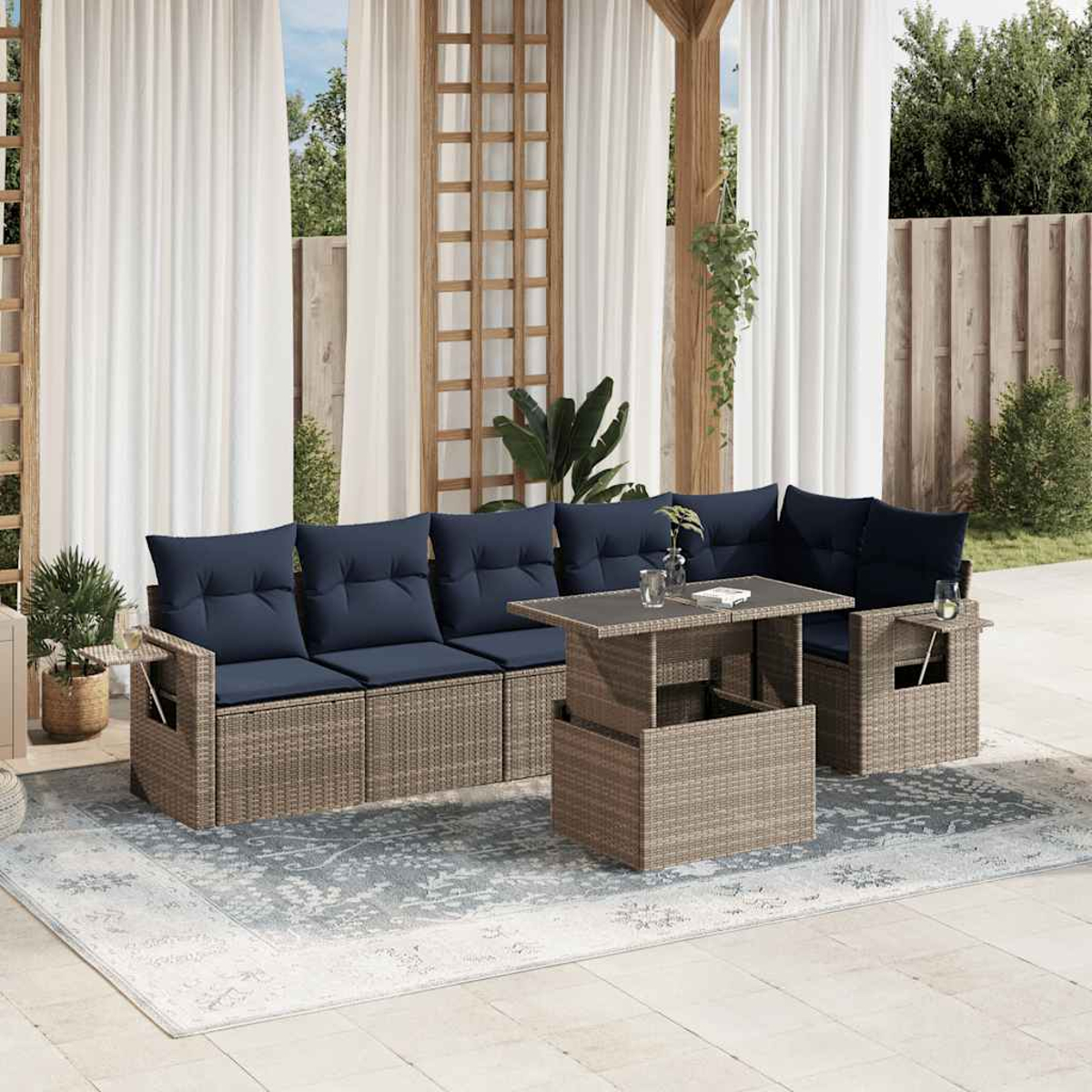 Garten-Terrassenset mit blauen Kissen und Korbflechtrahmen, einem Couchtisch und einem Teppich. Weiße Vorhänge und Holzstruktur im Hintergrund.