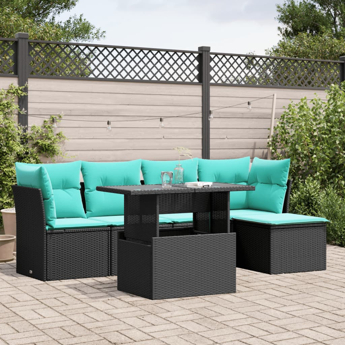 Terrassenmöbel mit türkisfarbenen Kissen und einem schwarzen Korbtisch. Ein Holzzaun und Pflanzen bilden den Hintergrund.