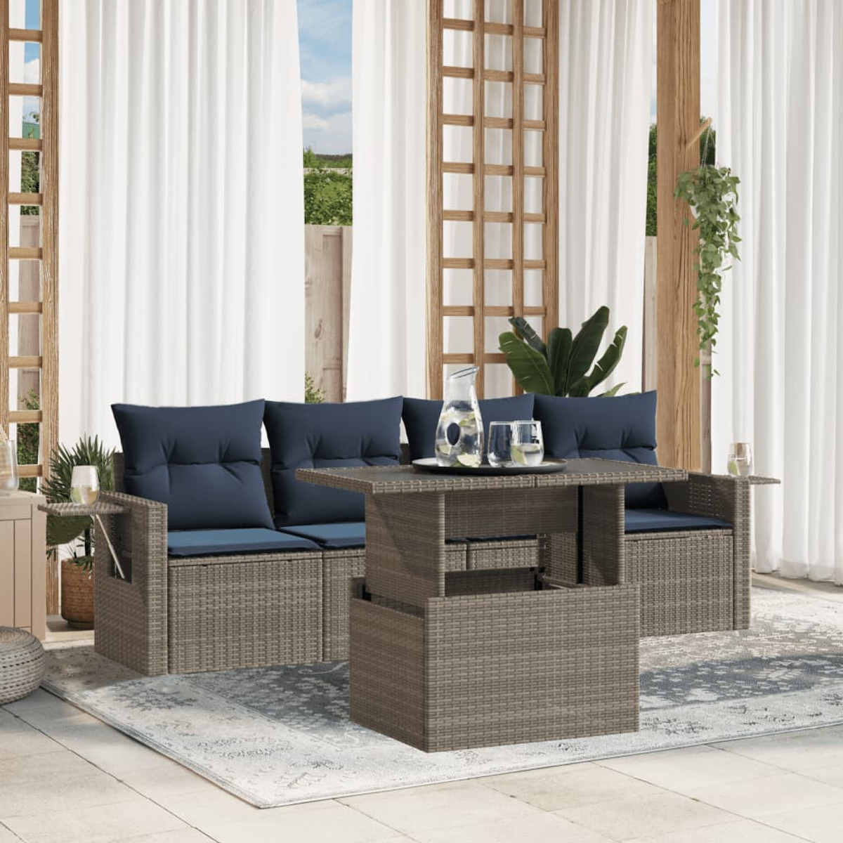 Garten-Set mit blauen Kissen, Couchtisch und Vorhängen. Ein Krug und Gläser stehen auf dem Tisch. Grüne Pflanzen im Hintergrund.