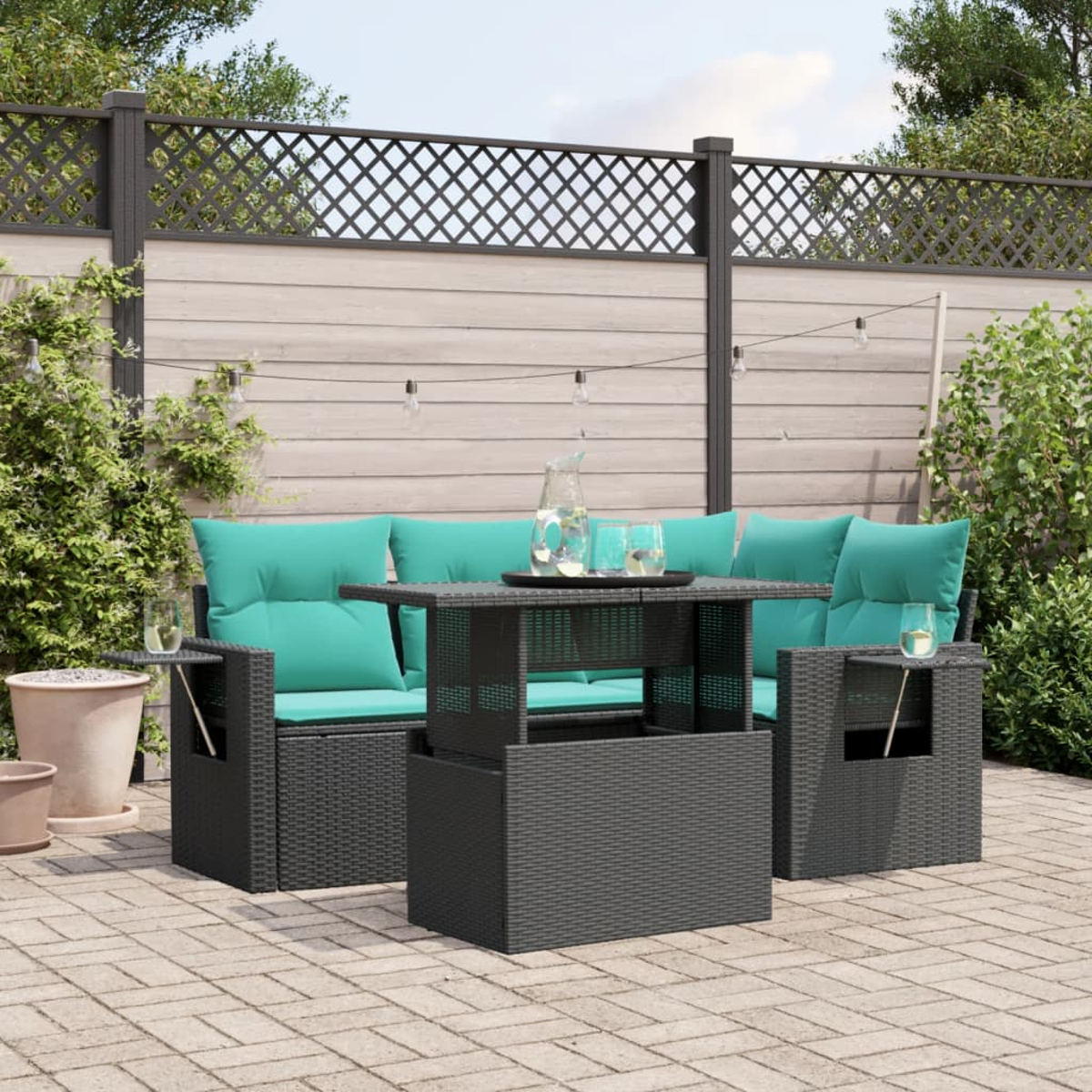 Terrassenset mit tealfarbenen Kissen, Tisch und Getränken. Im Hintergrund ein Zaun, Grün und Lichterketten.