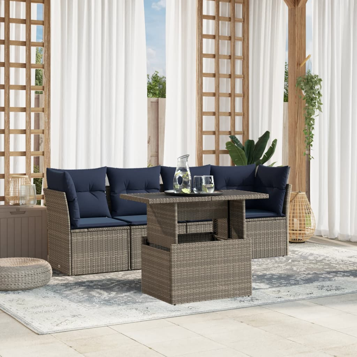 Terrassenset im Freien mit grauen Korbmöbeln, marineblauen Kissen, einem Tisch mit Hubfunktion und durchsichtigen weißen Vorhängen.
