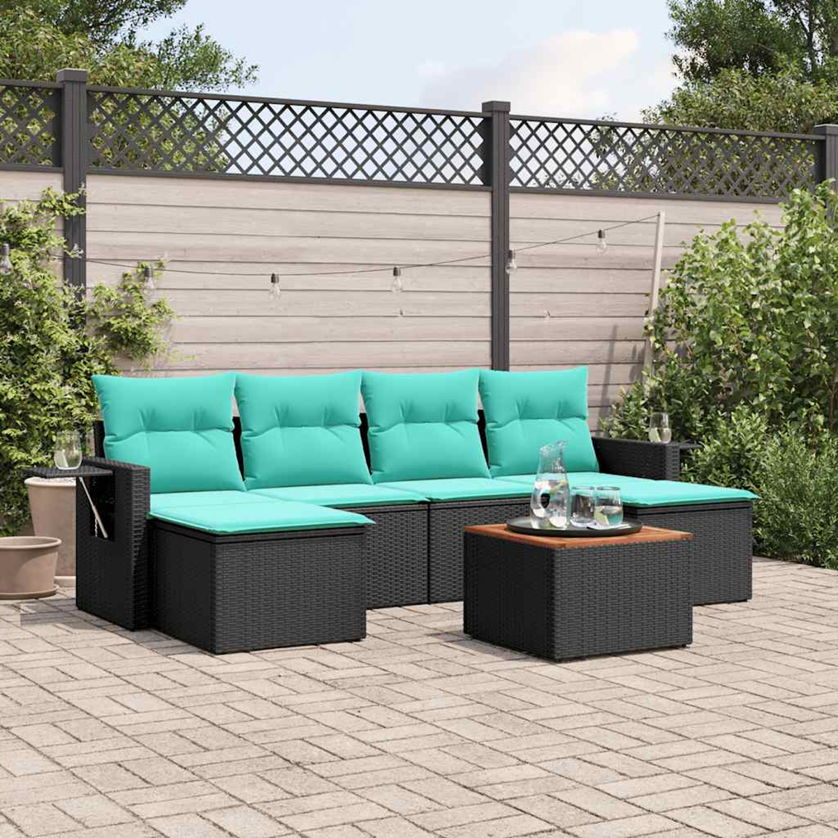 Outdoor-Sofa aus schwarzem Korbgeflecht mit türkisfarbenen Kissen und Kissen, einem kleinen Tisch und einem Couchtisch. In einem Garten mit Zaun.