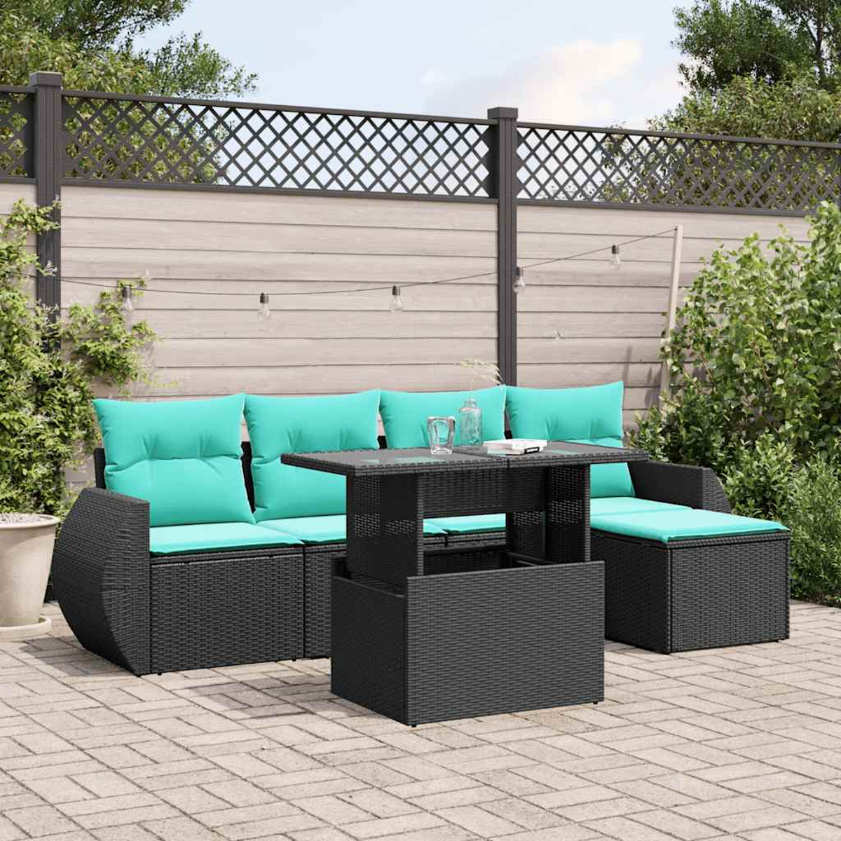 Terrassenmöbel-Set mit schwarzen Korbmöbeln, türkisfarbenen Kissen, einem Tisch mit Hubfunktion und einem Gitterzaun im Hintergrund.