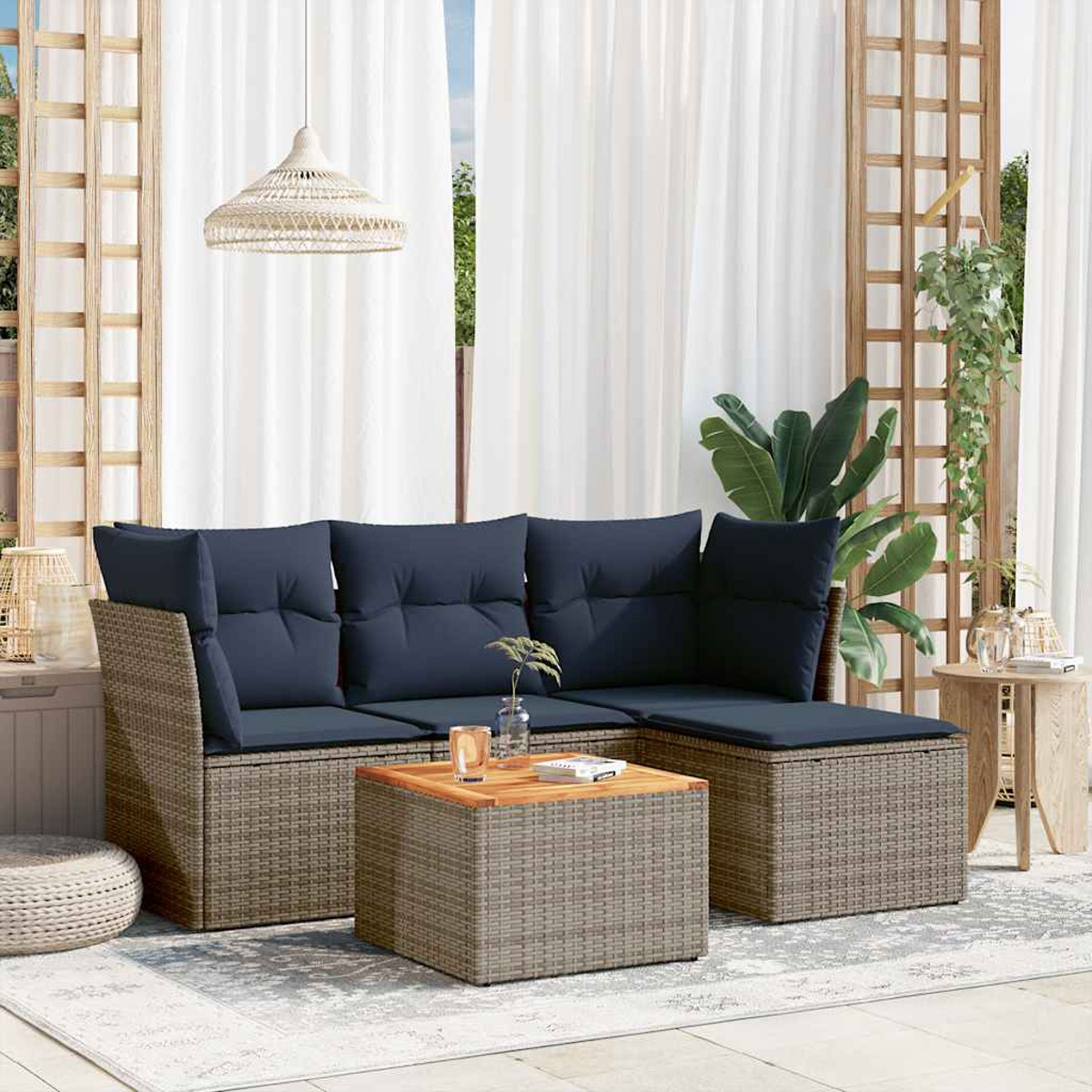 Outdoor-Sitzbereich mit Rattansofa, marineblauen Kissen und einem Couchtisch aus Holz. Weiße Vorhänge im Hintergrund.