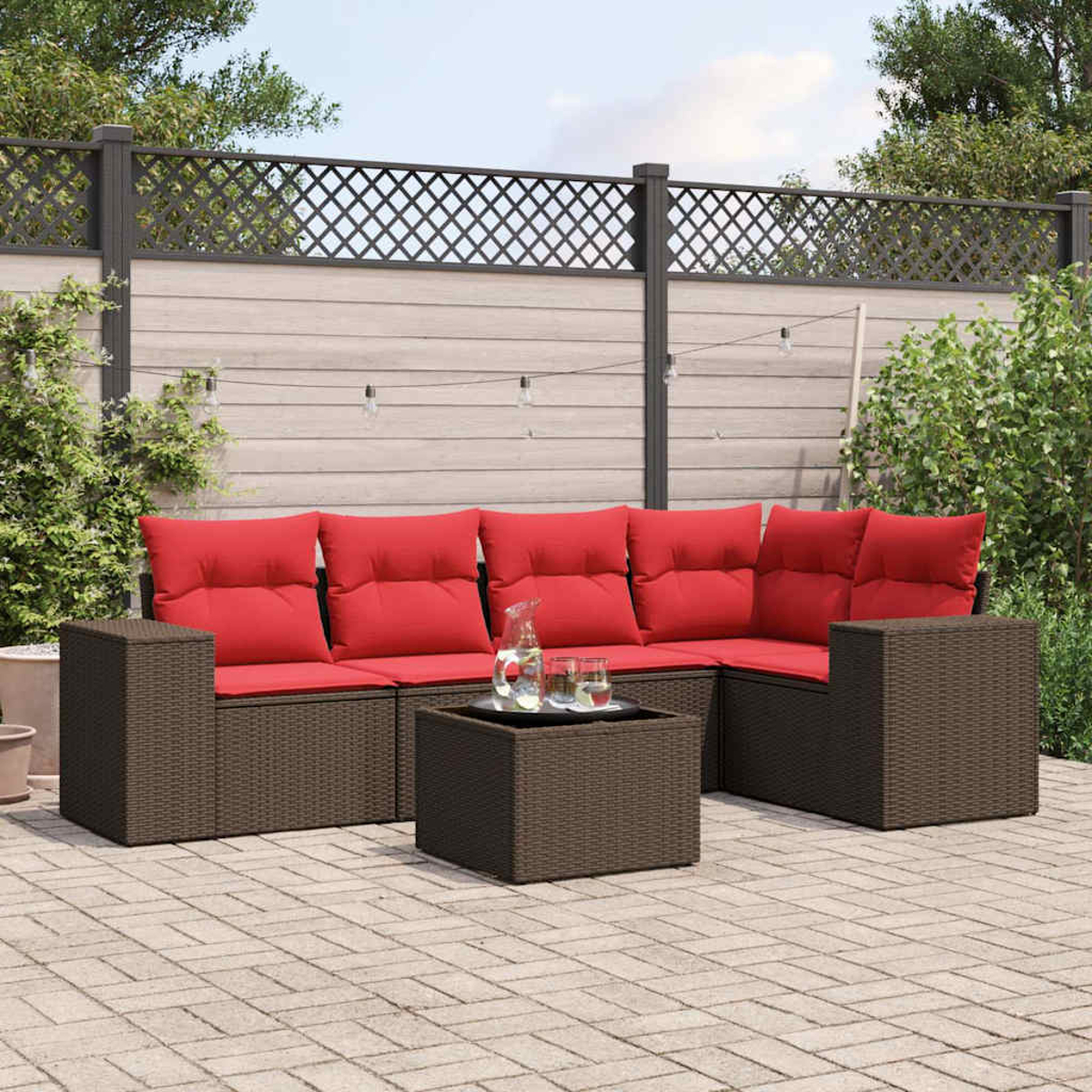 Garten-Lounge-Set mit roten Kissen und braunen Korbgewebeframes. Enthält einen Couchtisch und einen Hintergrund aus Zaun und Grün.