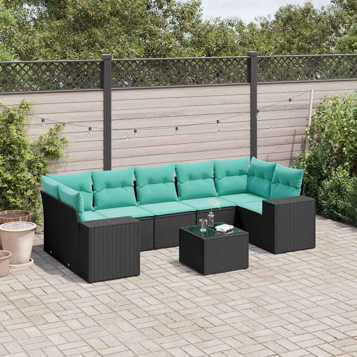 Garten-Sitzgruppe mit türkisfarbenen Kissen und schwarzem Rattangestell auf einer Ziegelterrasse mit kleinem Glastisch.
