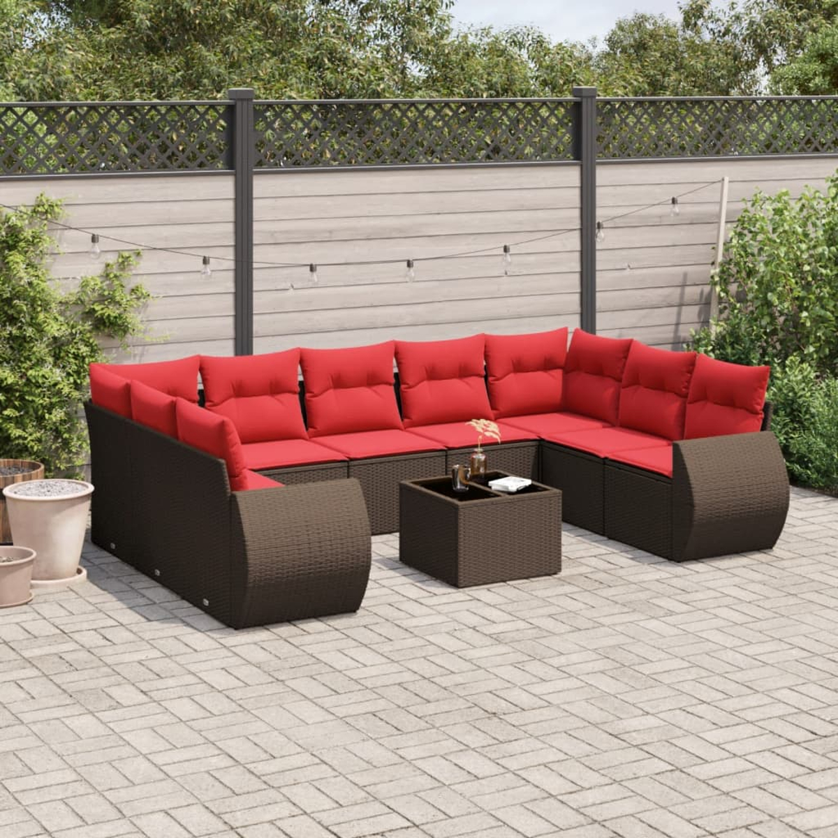 Ein Outdoor-Terrassenset mit roten Kissen, braunem Korbgewebe und einem passenden Couchtisch auf einer Ziegelterrasse. Ein Zaun und Pflanzen sind im Hintergrund.