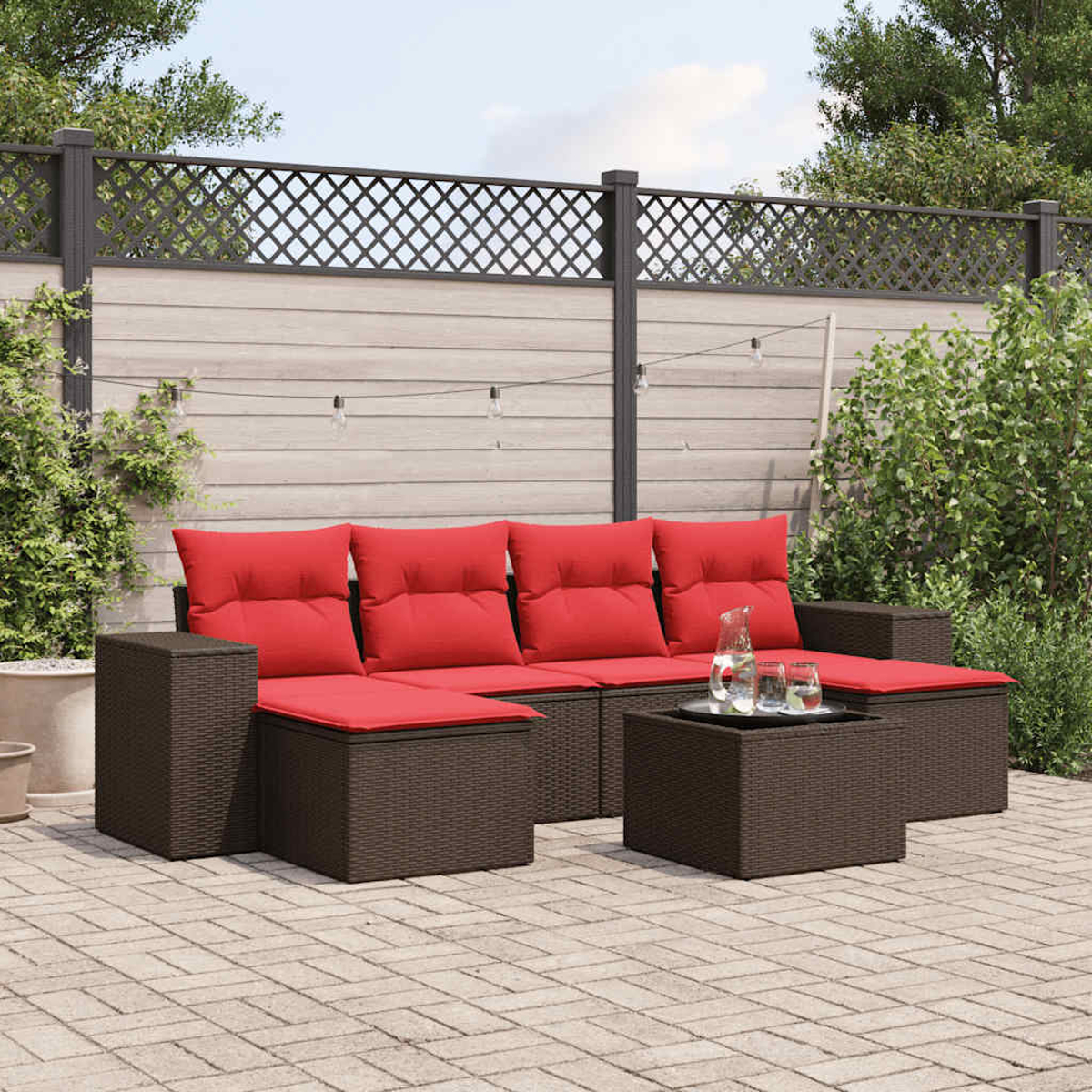 Sofá seccional exterior con cojines rojos y estructura de mimbre marrón, con mesa de centro a juego. En un patio de ladrillos.