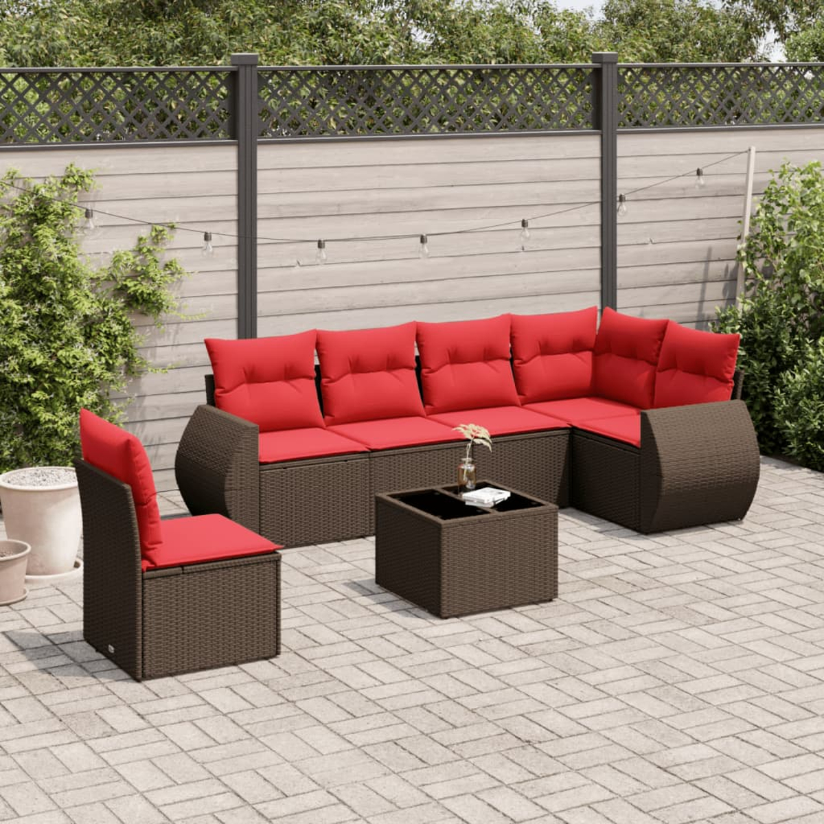 Outdoor-Terrassenset mit roten Kissen. Enthält ein Sofa, einen Stuhl und einen Tisch. Auf einer Steinterrasse mit Zaun und Pflanzen im Hintergrund.