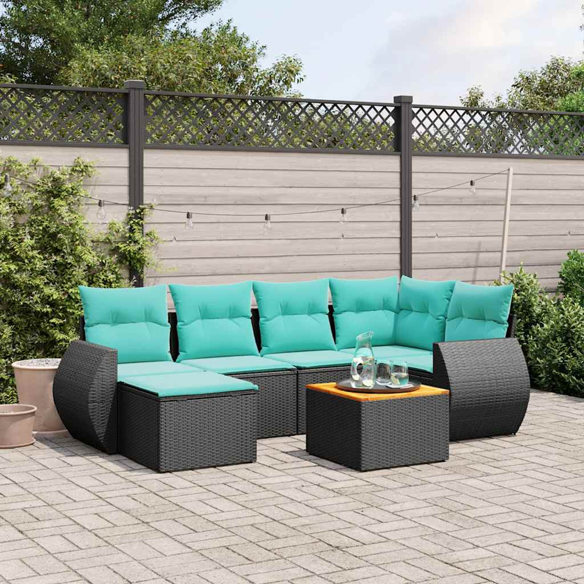 Garten-Sitzgruppe mit türkisfarbenen Kissen, einem kleinen Tisch mit Glaskrug und Gläsern und Holzzaun im Hintergrund.