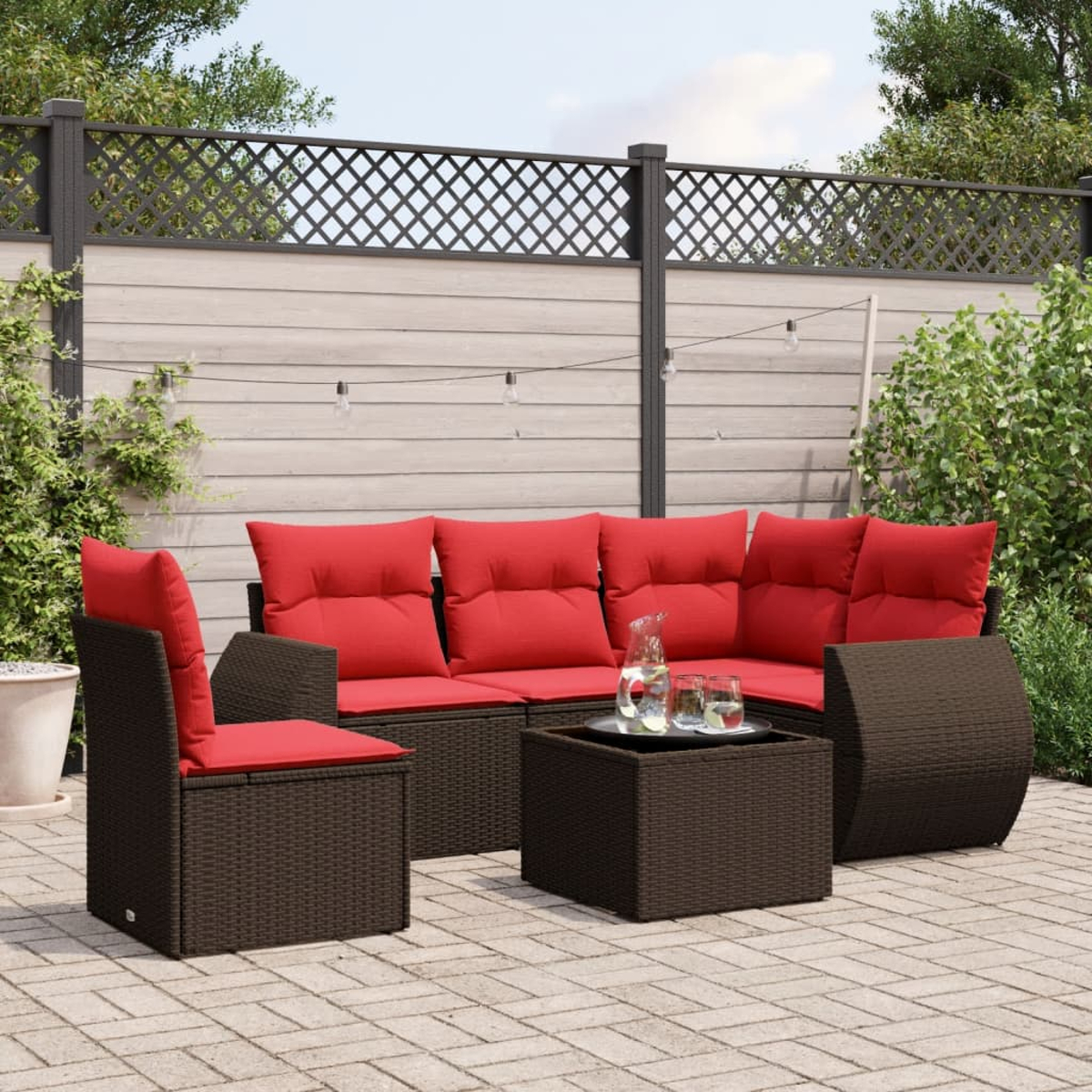 Garten-Terrassengarnitur mit braunen Korbmöbeln und roten Kissen. Enthält ein Sofa, einen Stuhl und einen Couchtisch. Im Hintergrund sind ein Zaun und Pflanzen.
