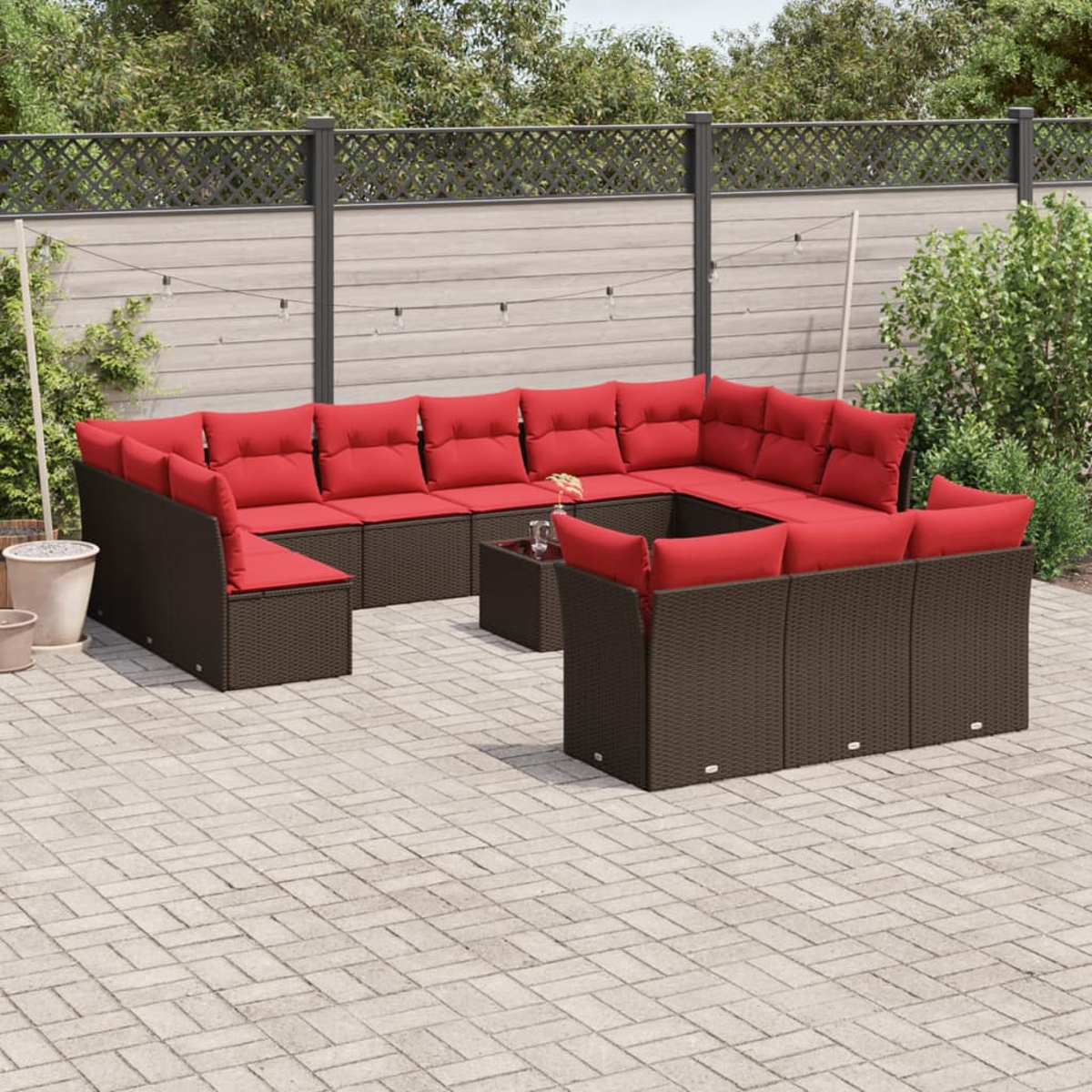Ein Ecksofa im Freien mit roten Kissen steht auf einer Ziegelterrasse. Ein kleiner Tisch steht in der Mitte. Grünpflanzen dahinter.