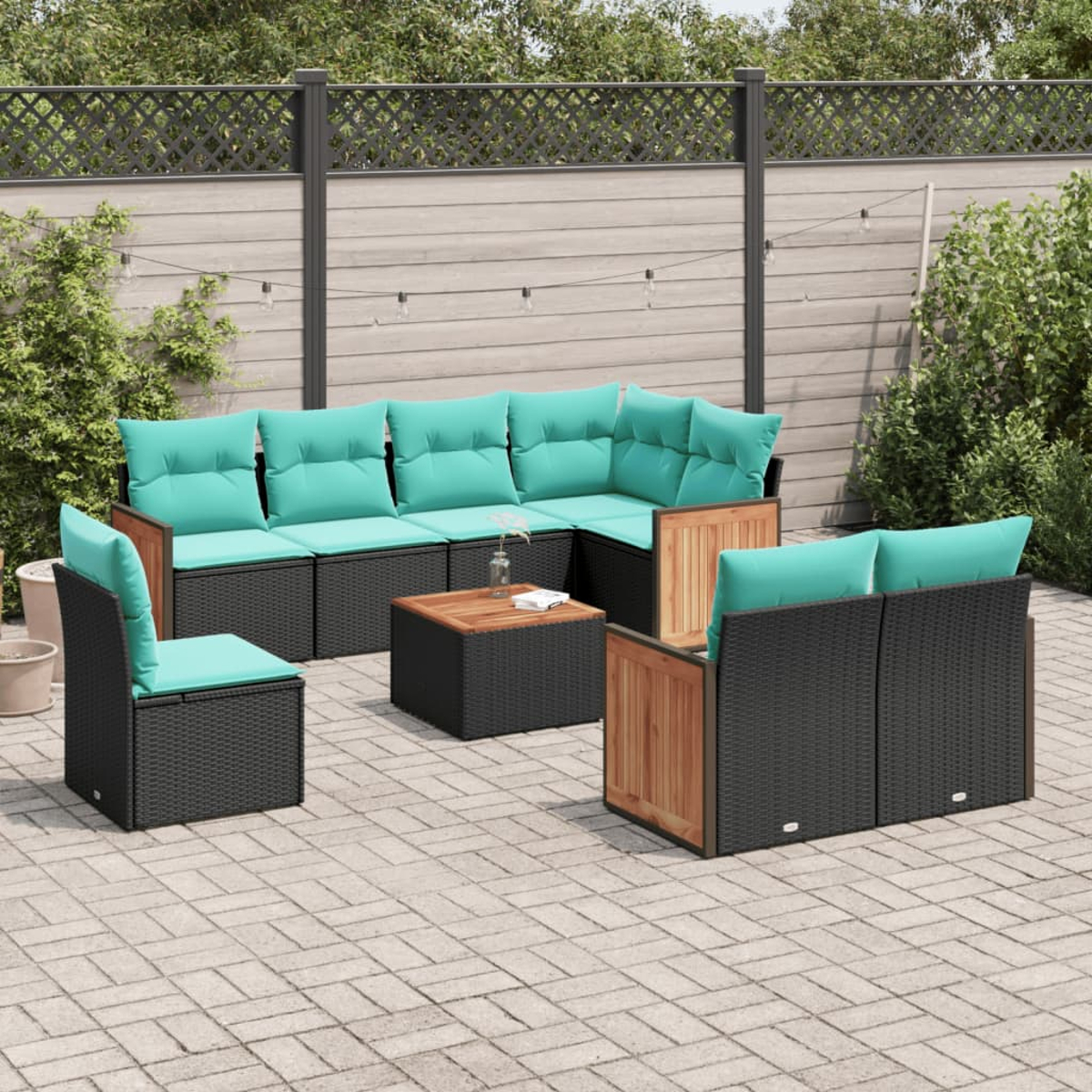 Terrassenset im Freien: schwarze Korbmöbel mit türkisfarbenen Kissen, Holzakzenten und einem kleinen Tisch auf einer Steinplatten-Terrasse.