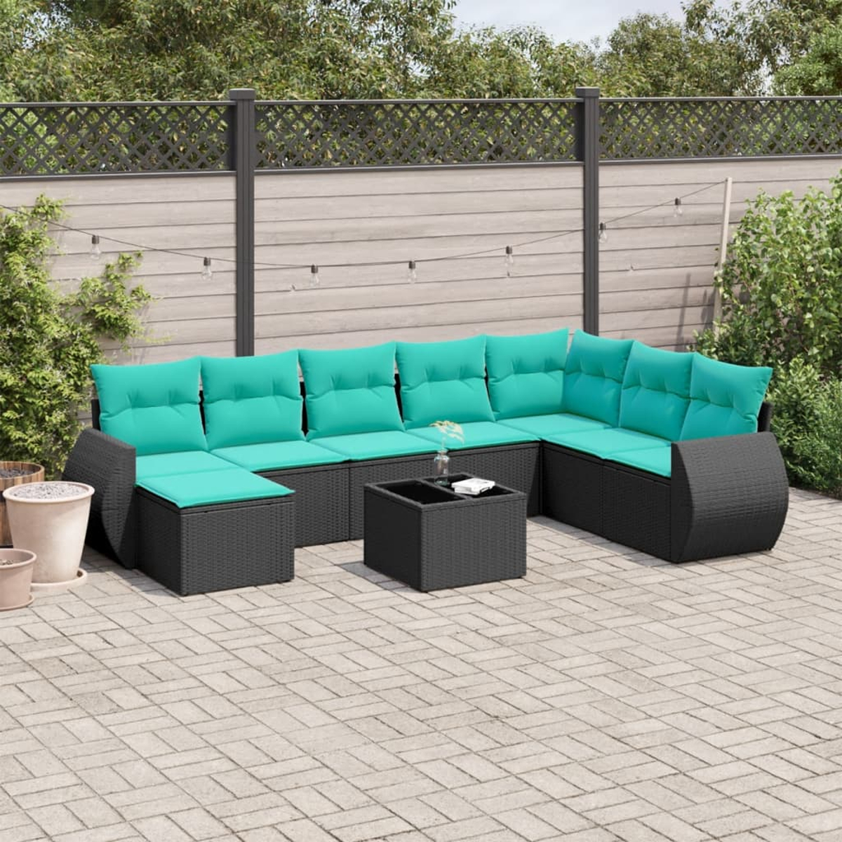 Ein Outdoor-Terrassenset mit schwarzen Korbmöbeln und türkisfarbenen Kissen auf einer Steinterrasse. Ein kleiner Tisch und Pflanzen sind in der Nähe.