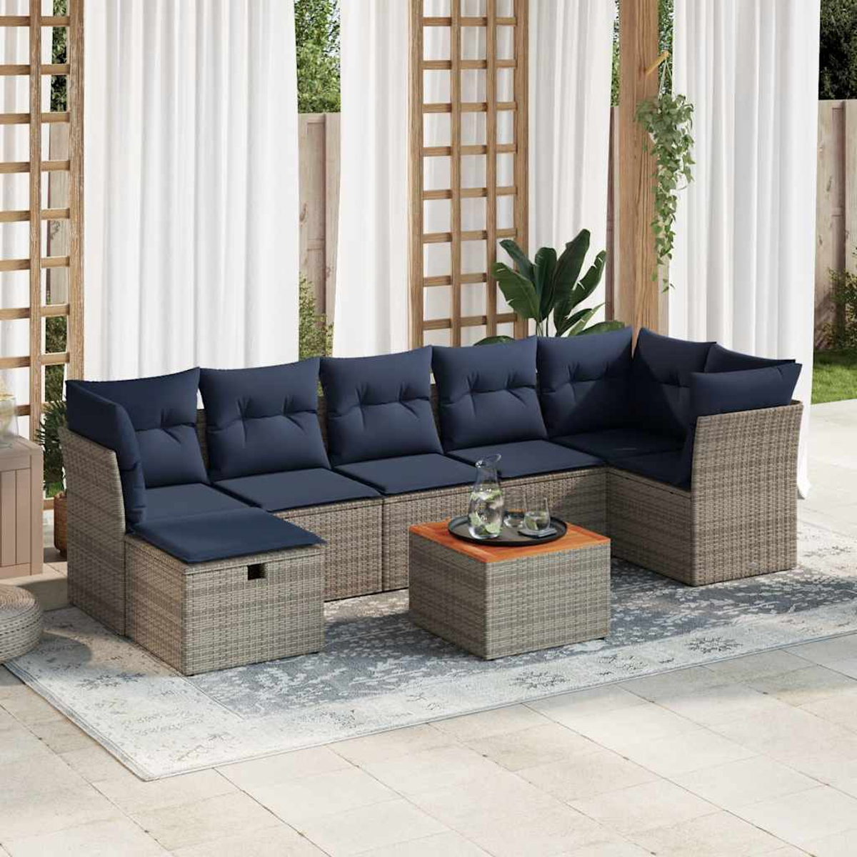 Outdoor-Ecksofa mit marineblauen Kissen und einem kleinen Tisch mit Getränken, auf einem Teppich, mit Vorhängen und Holzgitter im Hintergrund.