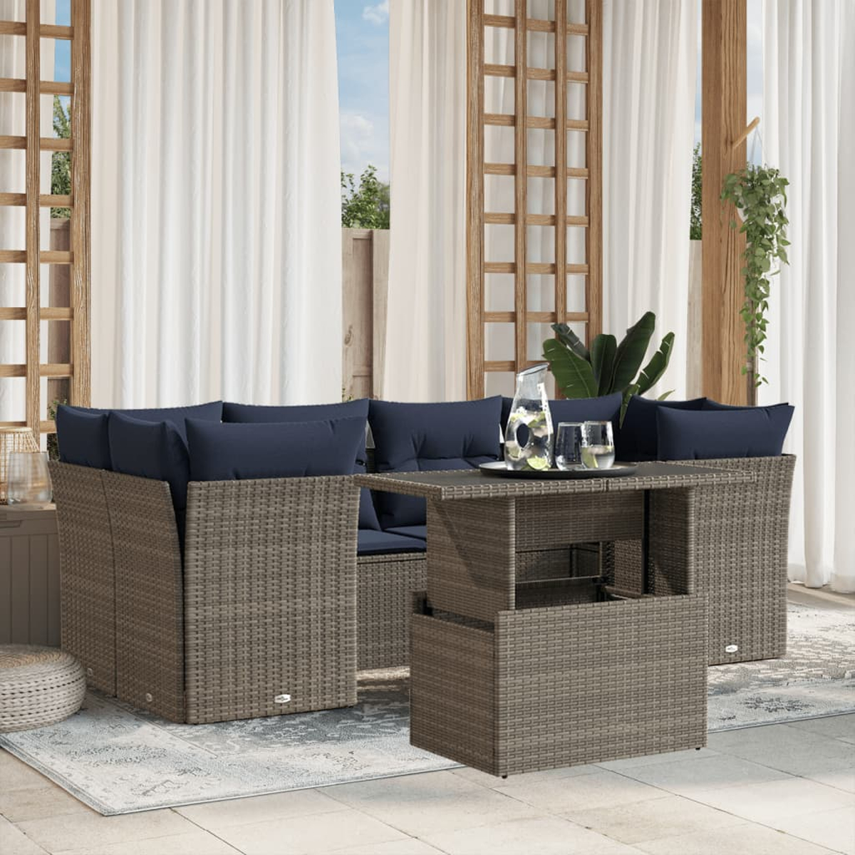 Gartenmöbel-Set aus Korbgeflecht mit blauen Kissen. Ein Tisch mit Gläsern und einem Krug. Weiße Vorhänge und Holzrahmen.