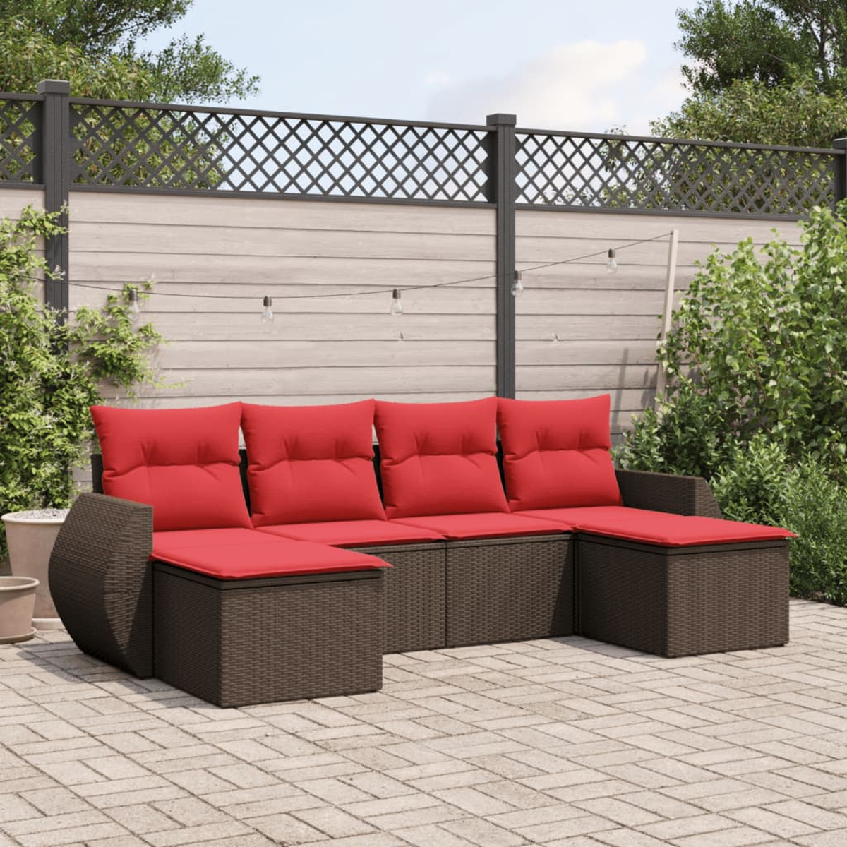 Outdoor-Ecksofa mit roten Kissen auf einer Ziegelterrasse. Braune Korbmöbel vor einem Holzzaun.